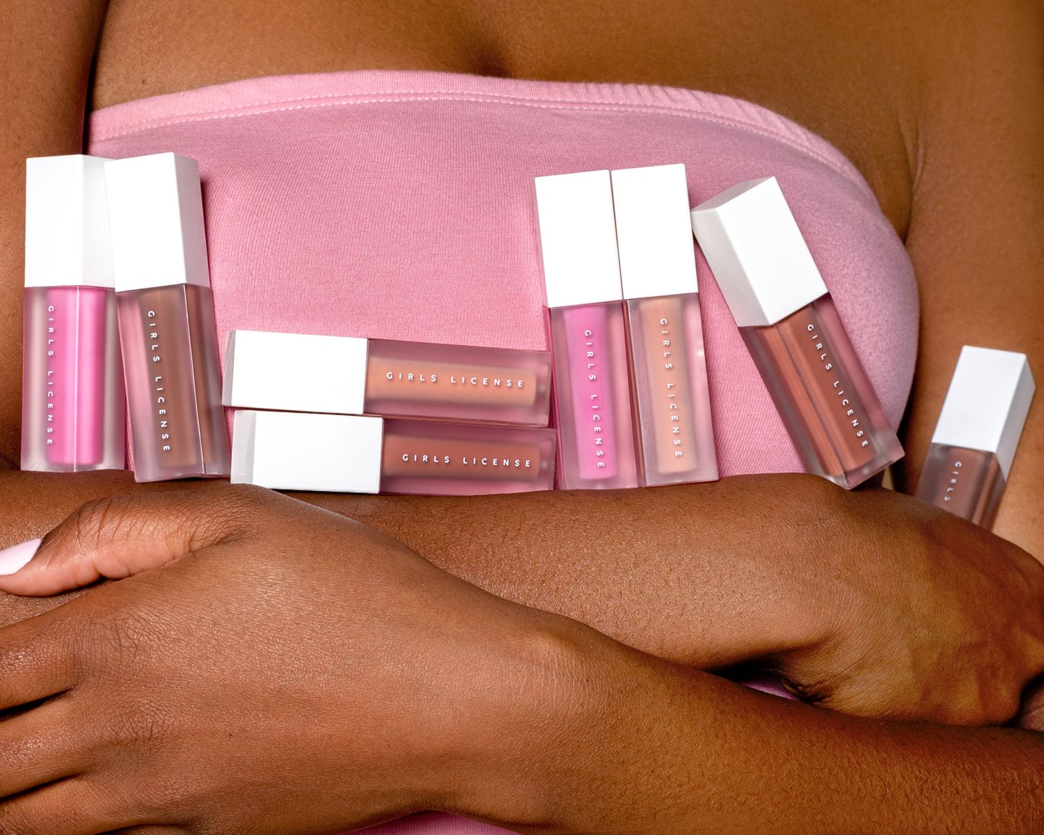 A row of pink makeup products being held against a dark brown surface.
