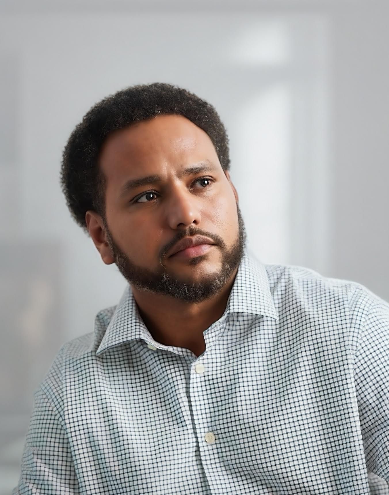 Professional headshot of man in checkered shirt against soft gray background.