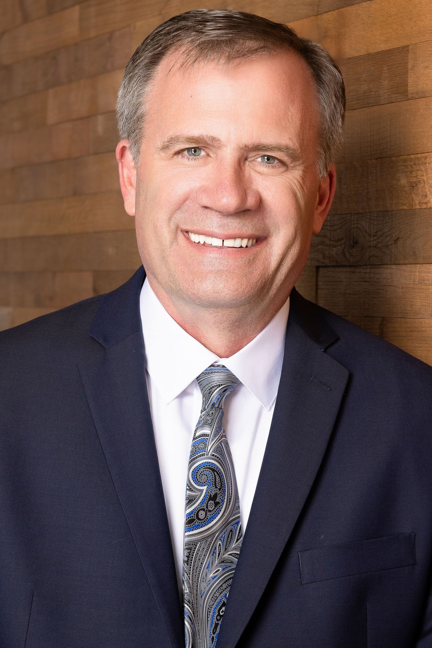 Professional business portrait against wooden backdrop wearing navy suit.