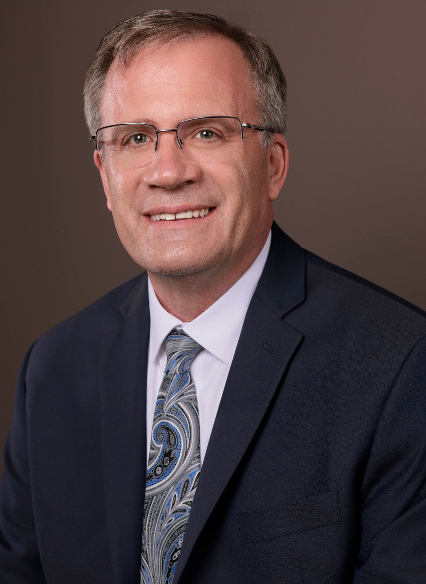 Business portrait of an executive in formal attire against brown background.