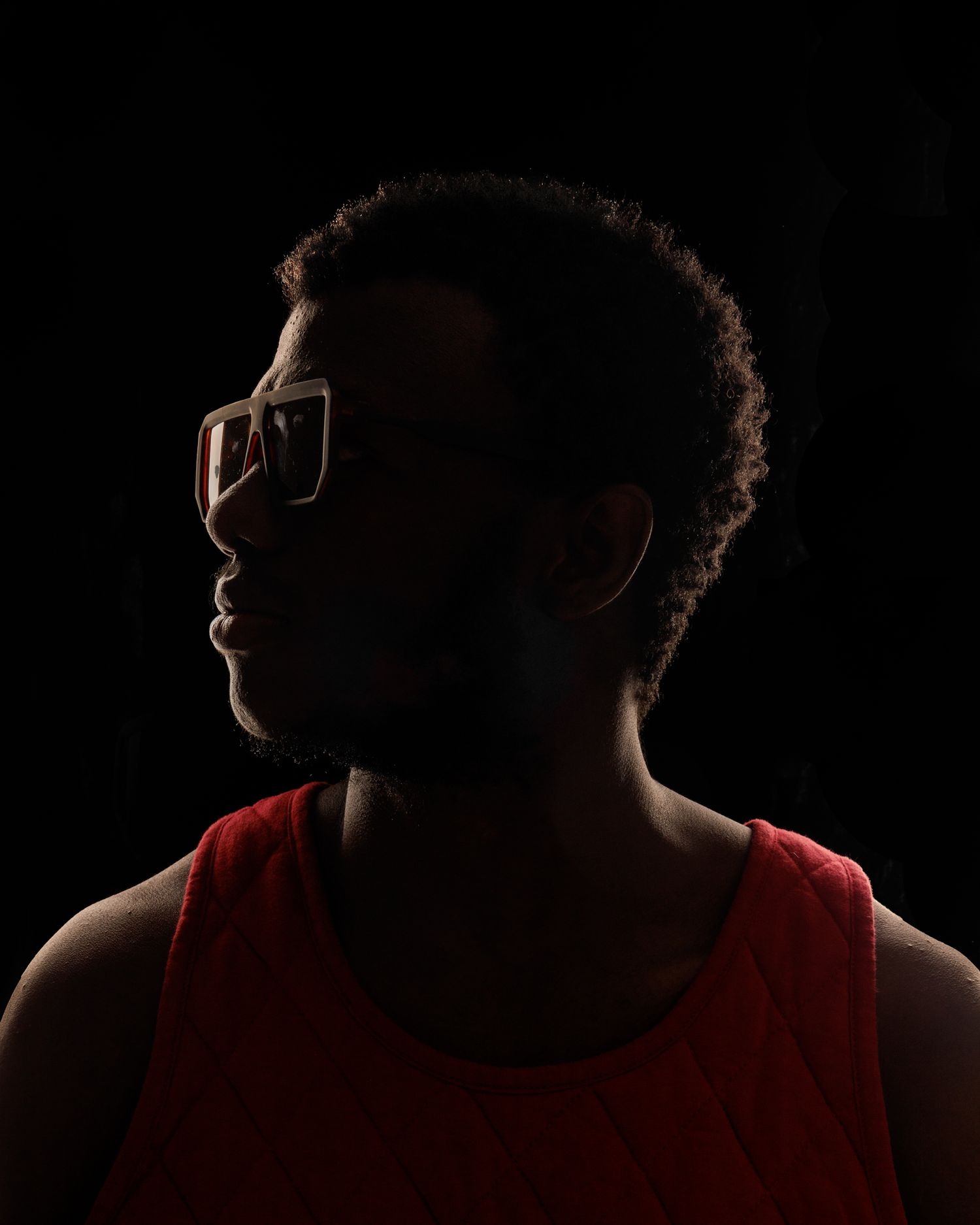 Moody side profile portrait with dramatic shadows highlighting glasses and red tank top.