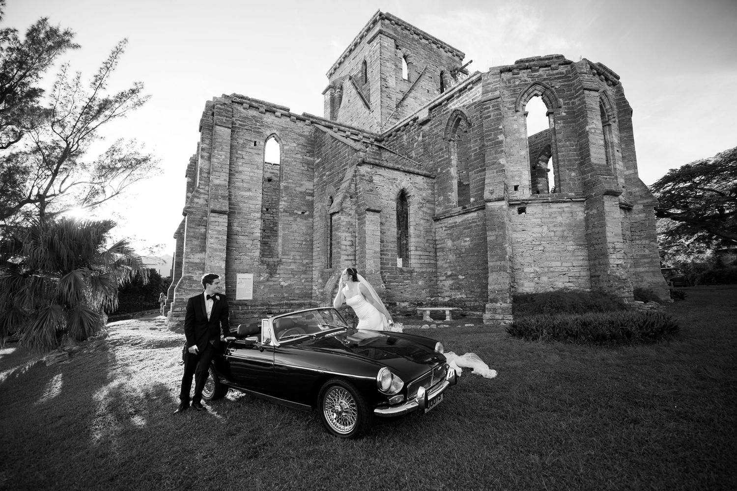 Classic car parked outside historic stone church ruins in black and white.