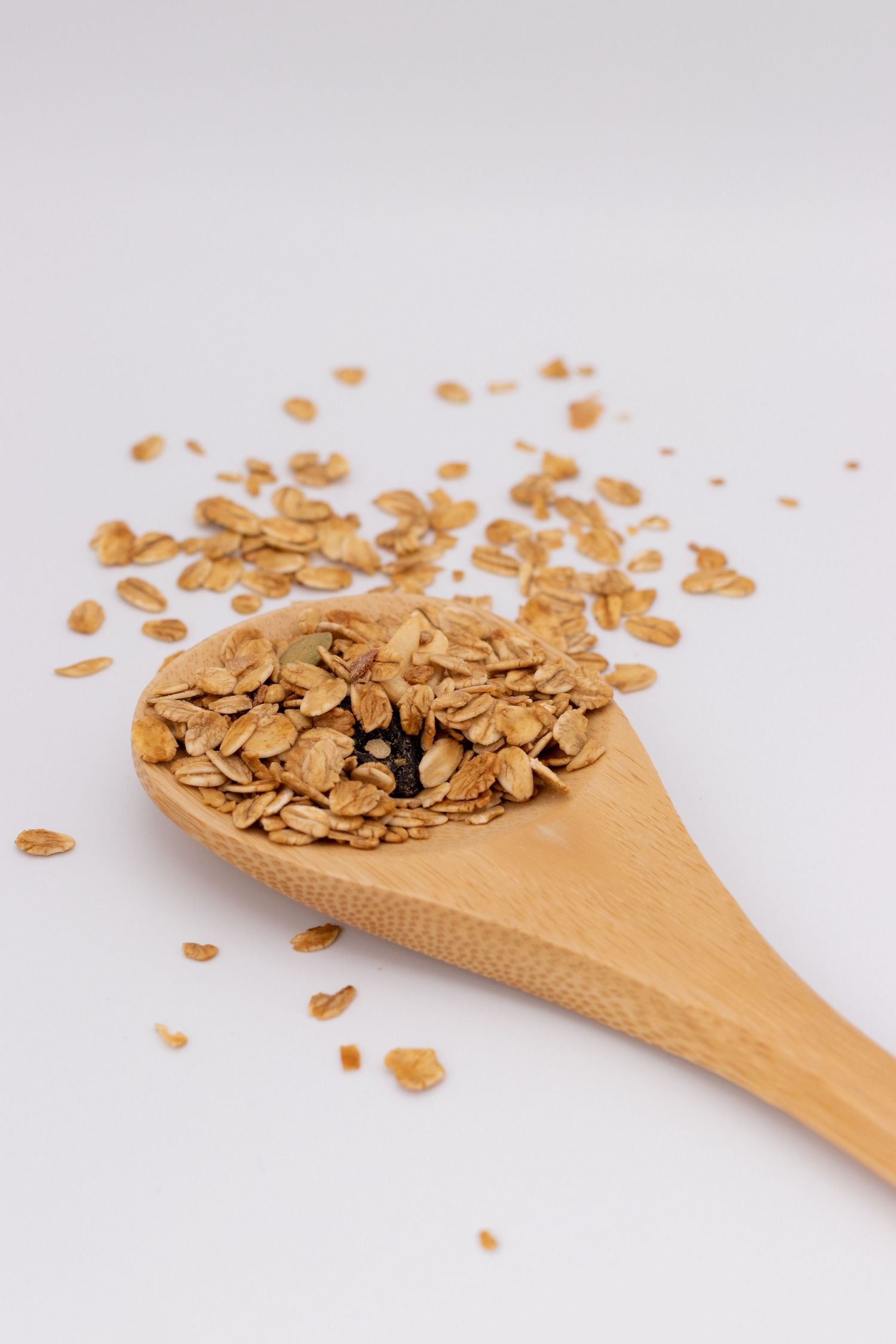 Wooden spoon filled with golden oat flakes on white background.