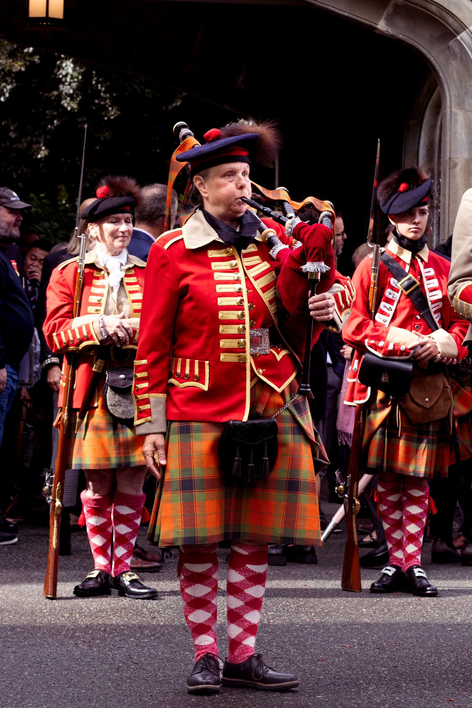 Performers in bright red uniforms with checkered pants playing instruments during a traditional ceremonial procession.