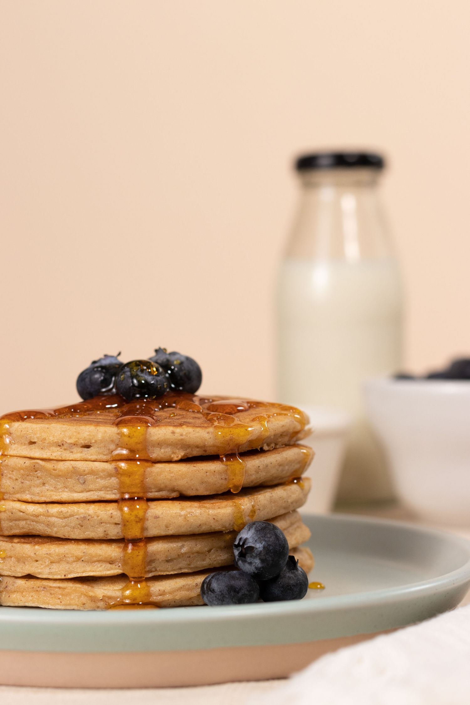 Stack of golden pancakes with maple syrup and blueberries on a light blue plate.