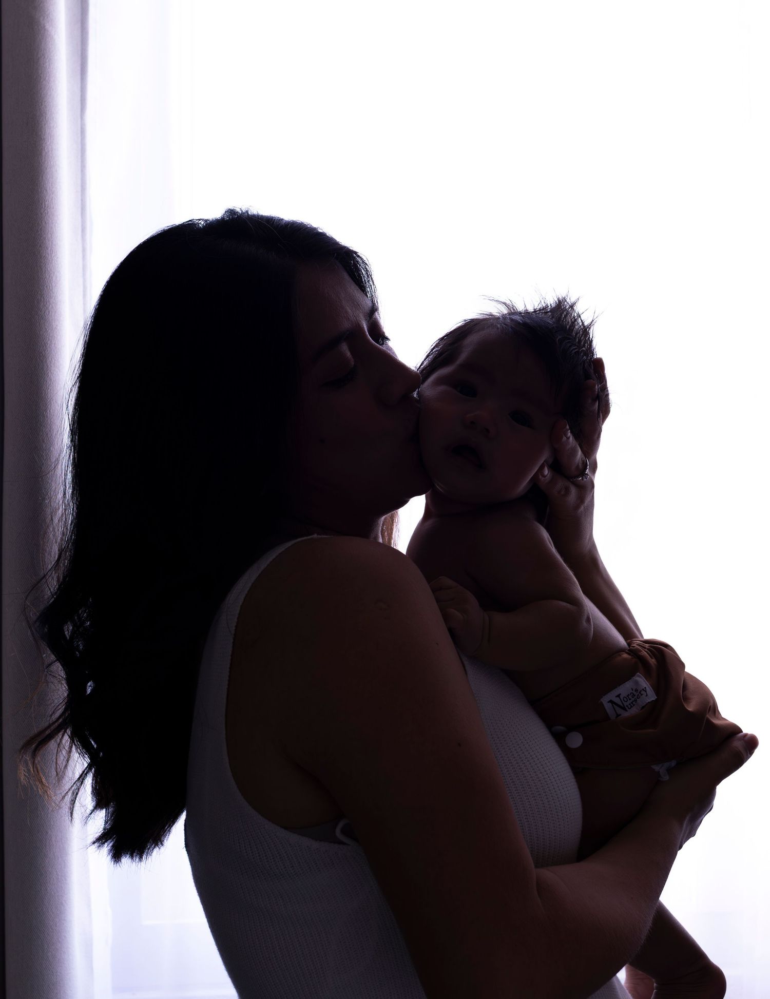 Silhouette of parent and baby sharing tender moment against backlit window.