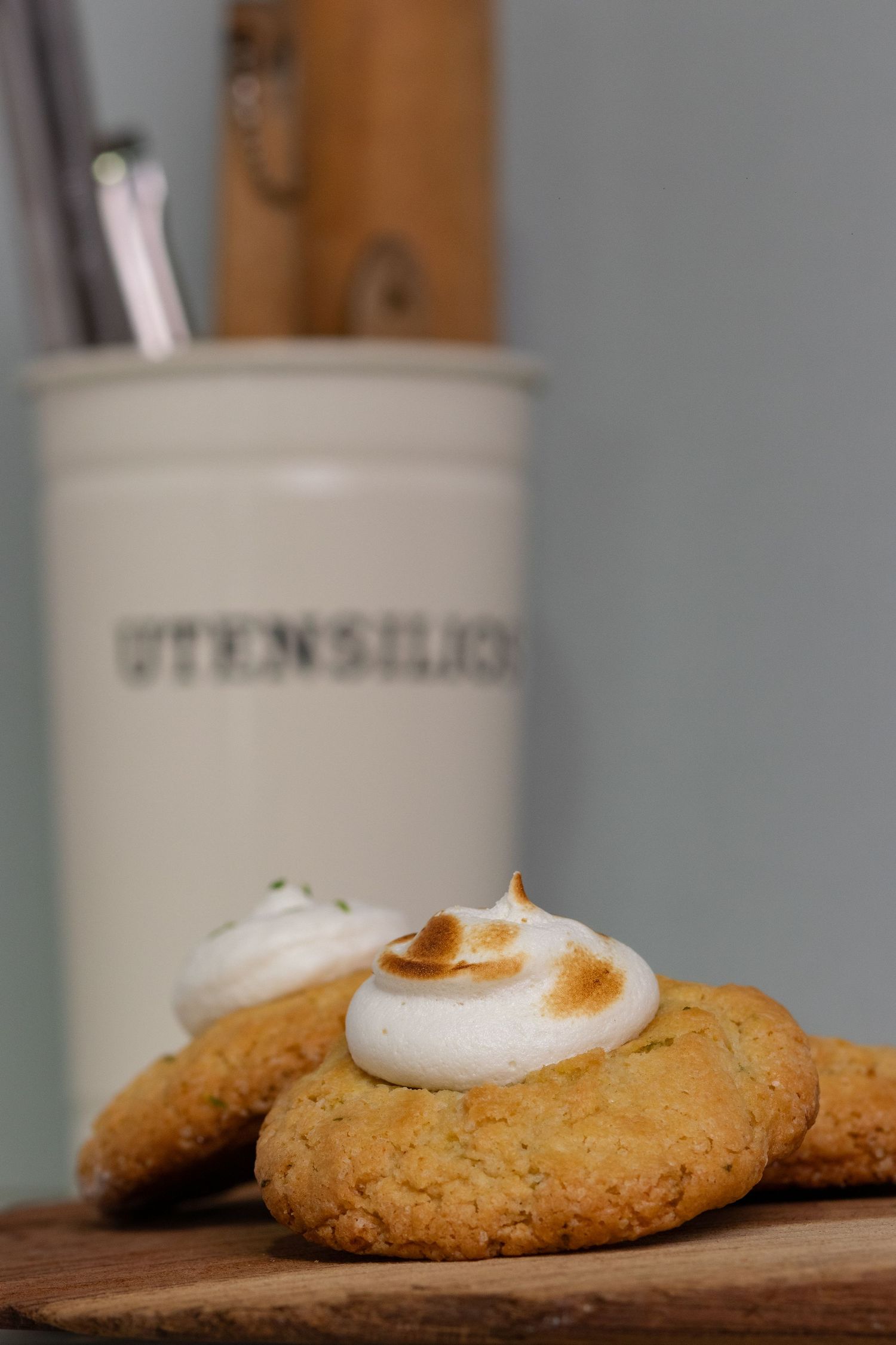 Homemade cookies with white frosting displayed on a wooden board near kitchen utensils.