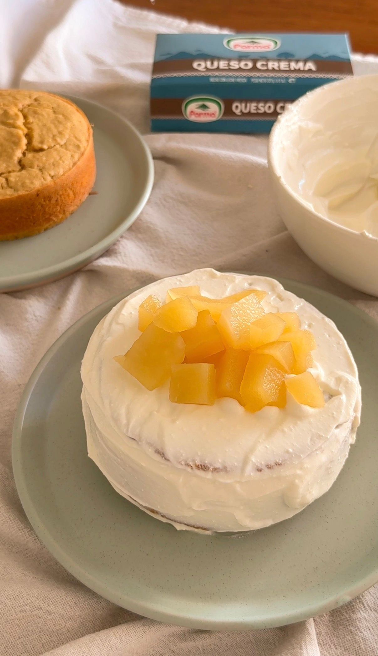 Mini cream cake topped with diced peaches, made with Queso Crema cheese, displayed on a sage green plate.