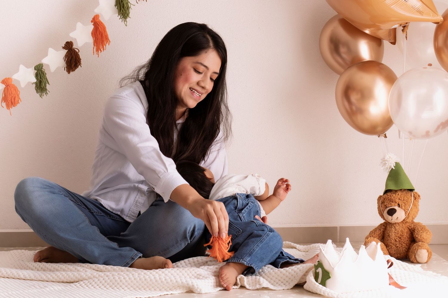 Woman in white shirt and jeans sits on floor with autumn leaves and copper balloons in cozy home setting.