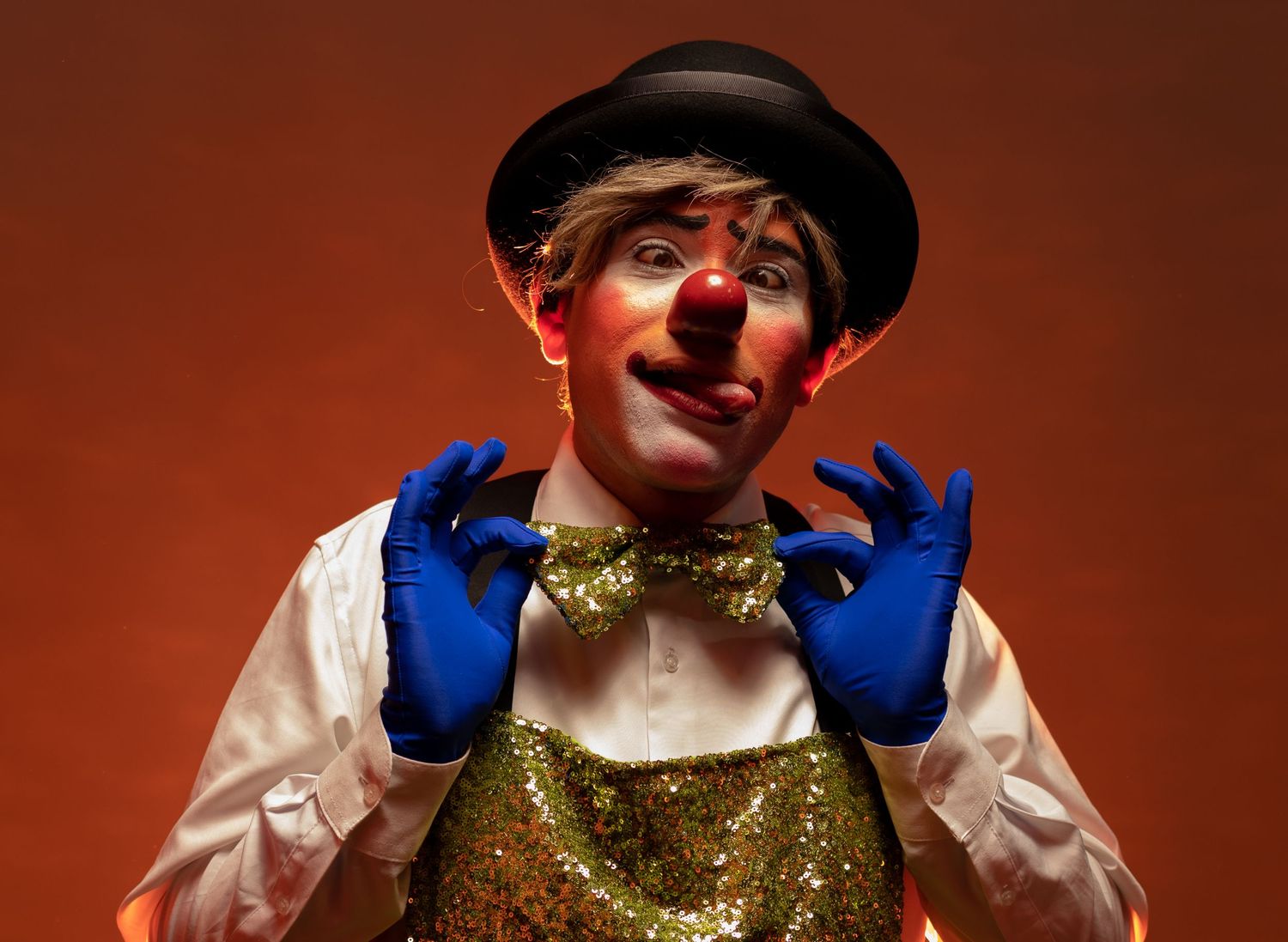 Clown in sparkly costume and blue gloves making expressive gesture.