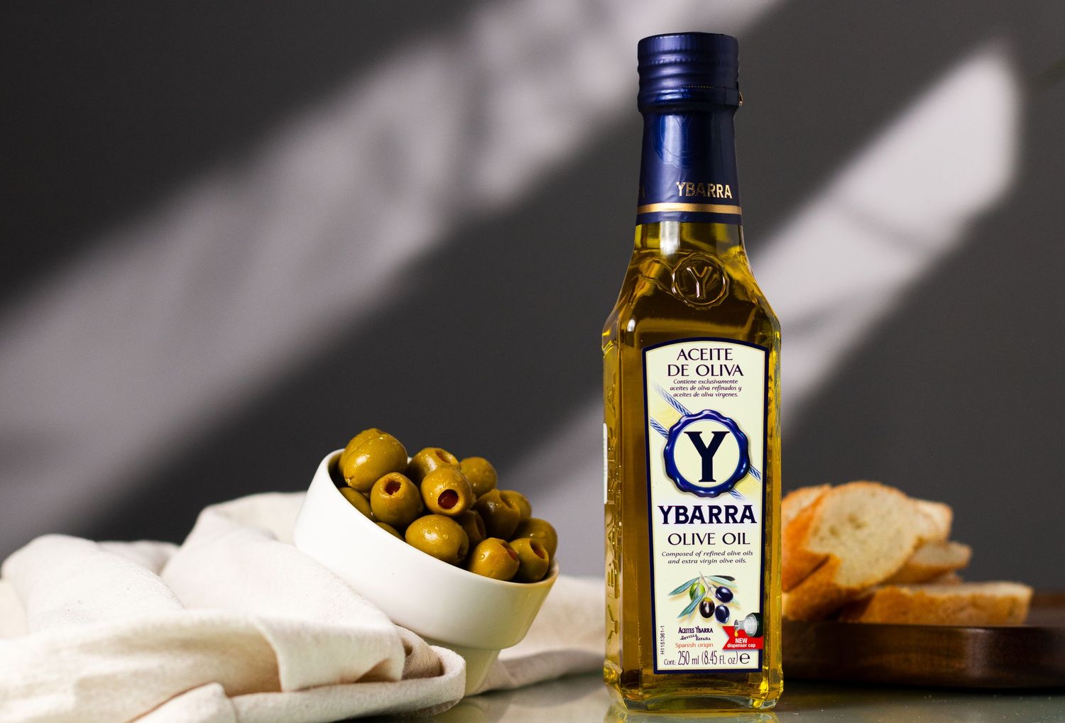 Artistically styled olive oil bottles with bread and olives in dramatic lighting.