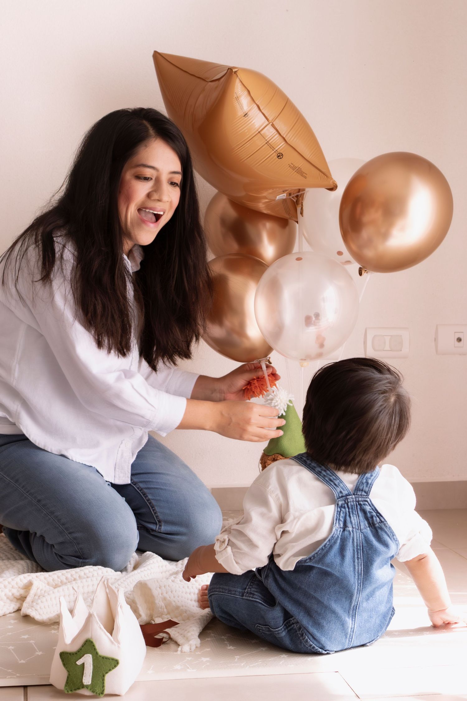 A joyful celebration with copper and pink balloons, denim overalls, and a number one decoration on the floor.