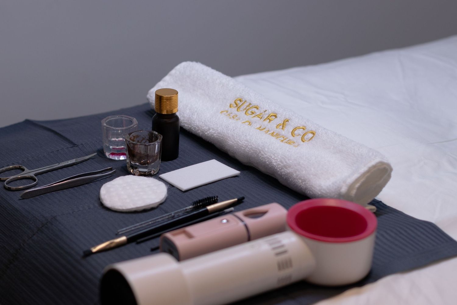 Sugar & Co beauty treatment table with professional tools, towel, scissors, brushes, and skincare products neatly arranged.