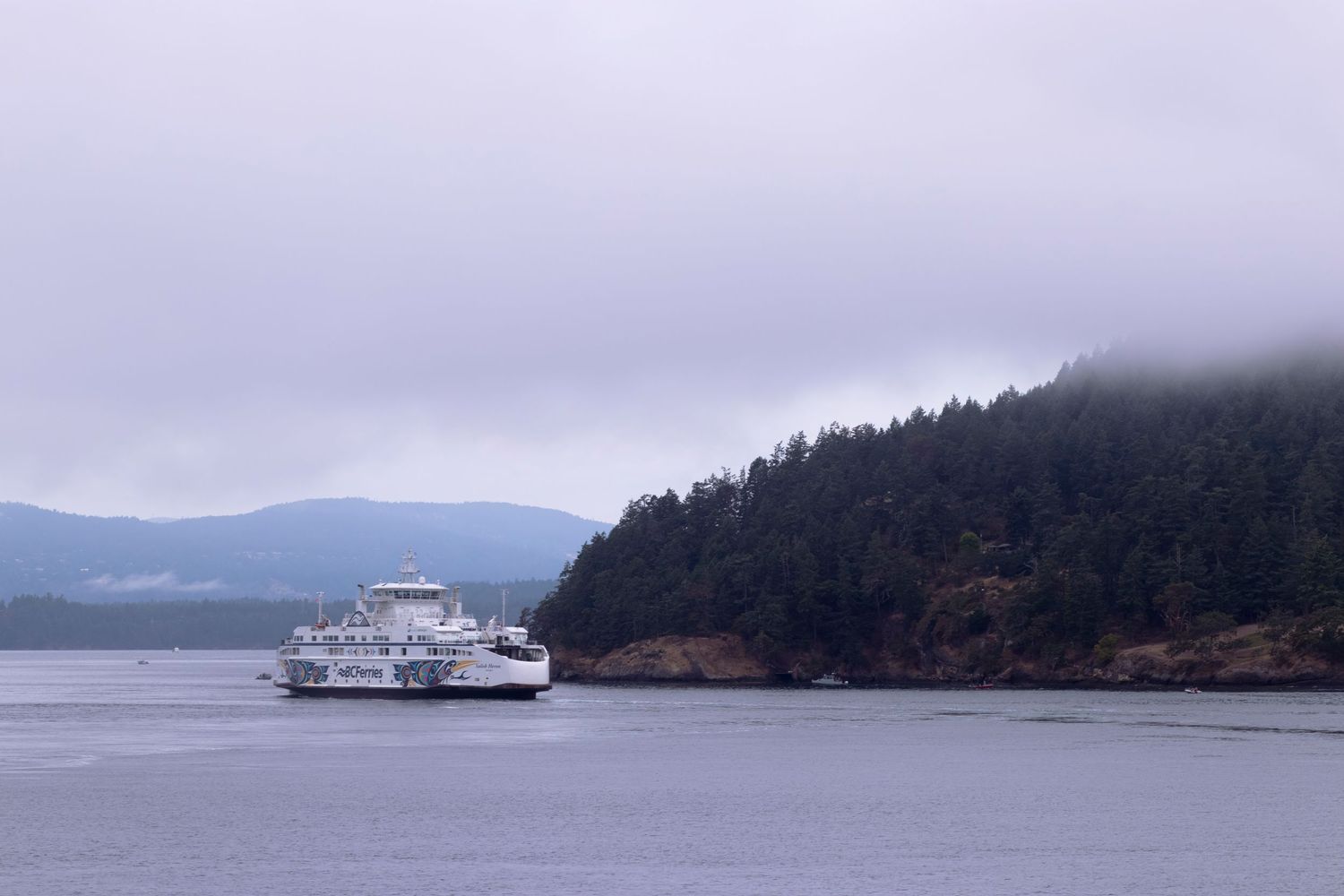 A Washington State ferry travels through the misty waters of Puget Sound with evergreen-covered islands in the background.