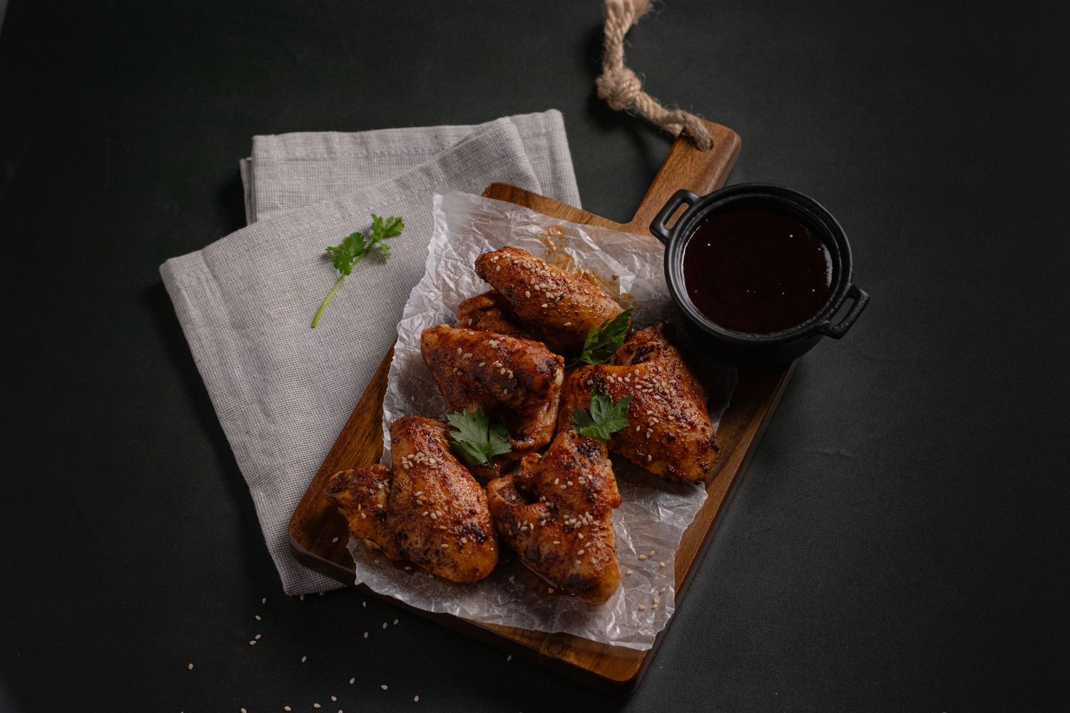 Dark moody food photography of crispy fried chicken pieces with sauce and garnish.