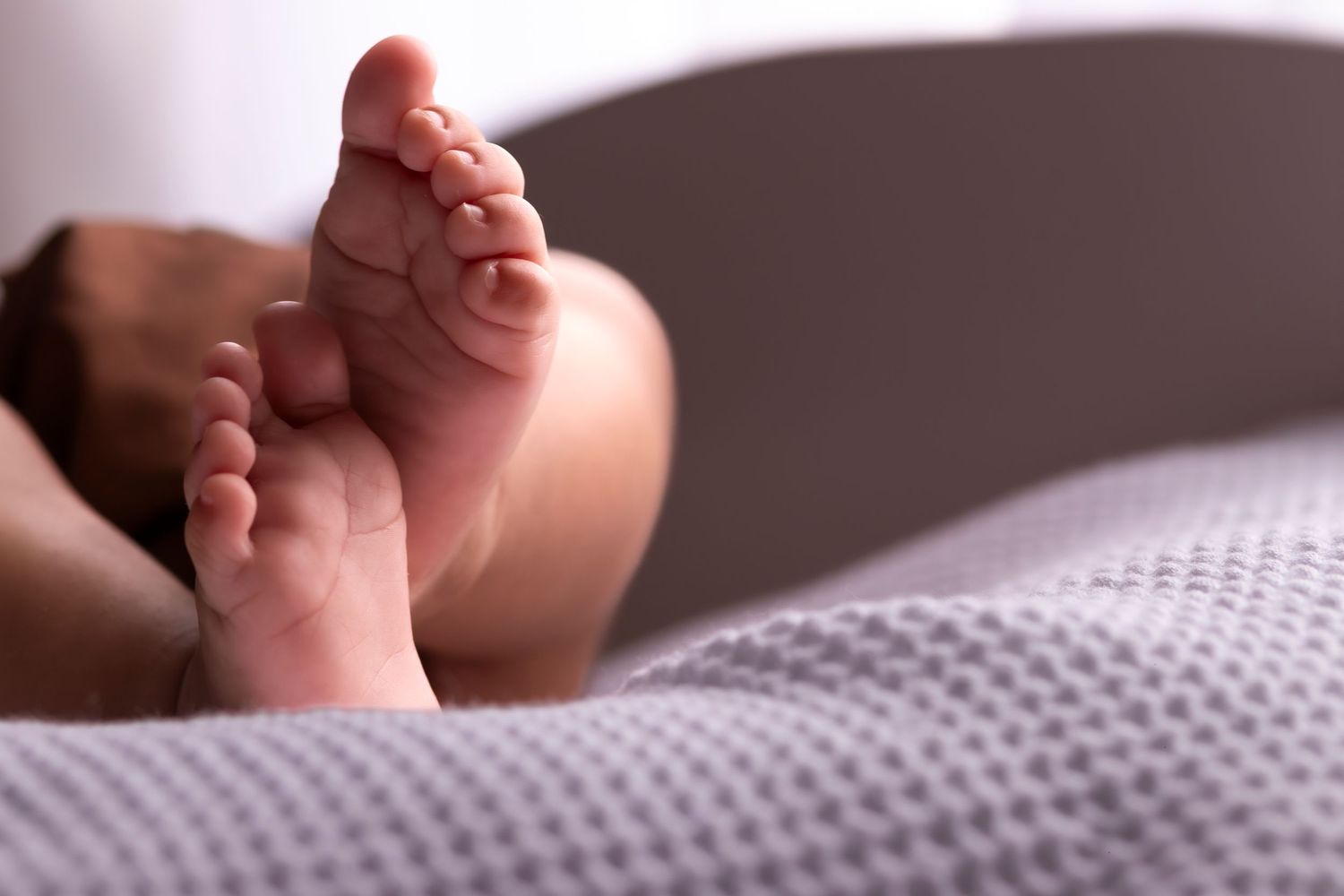 Close-up of tiny baby feet resting on a textured white blanket.