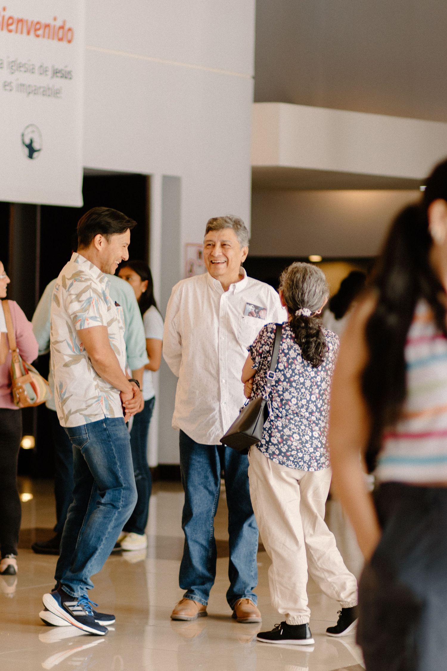 People socializing in a church lobby with a bienvenido welcome sign in a Spanish-speaking congregation.