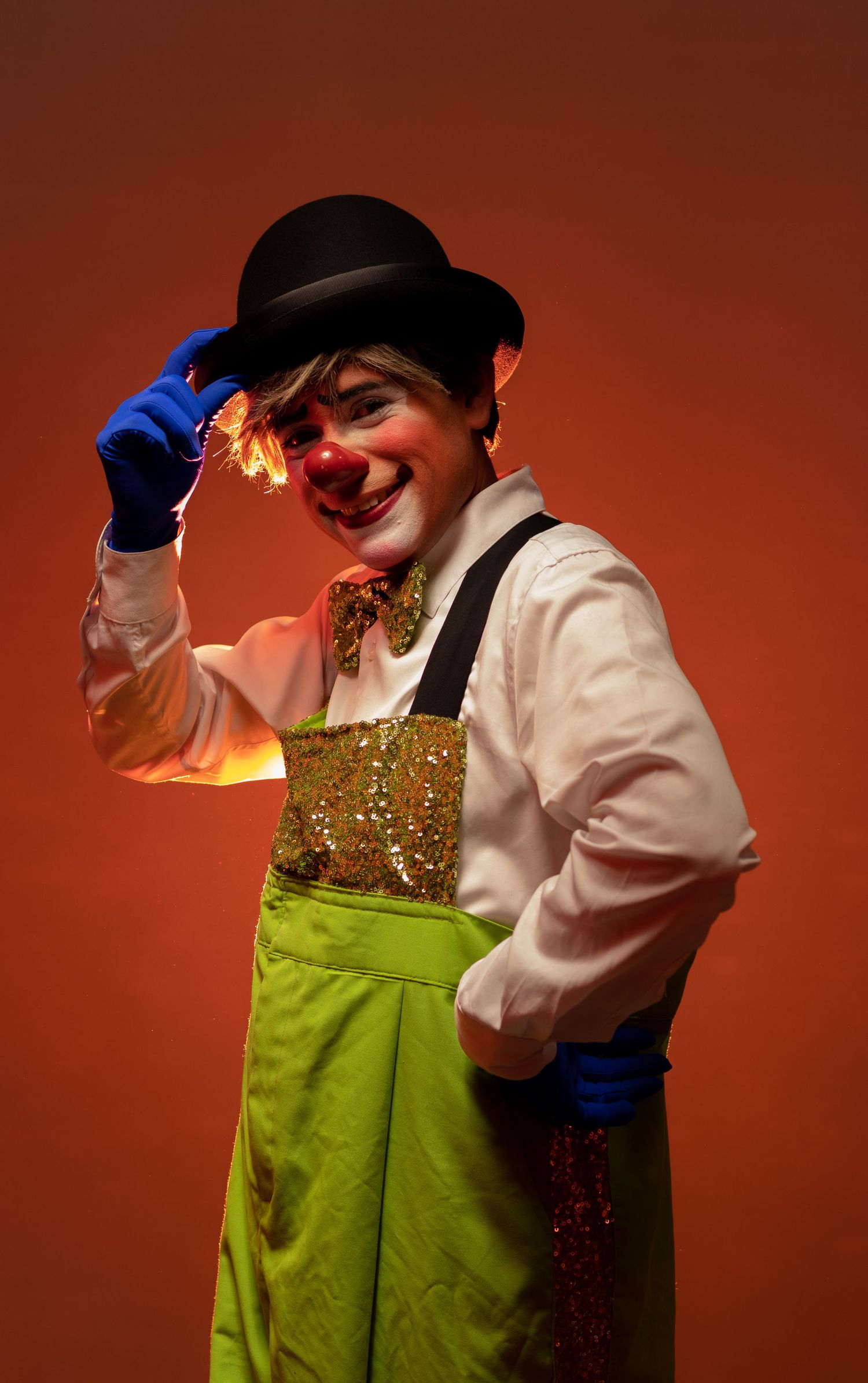 Circus performer in bowler hat and sparkly costume against red backdrop.