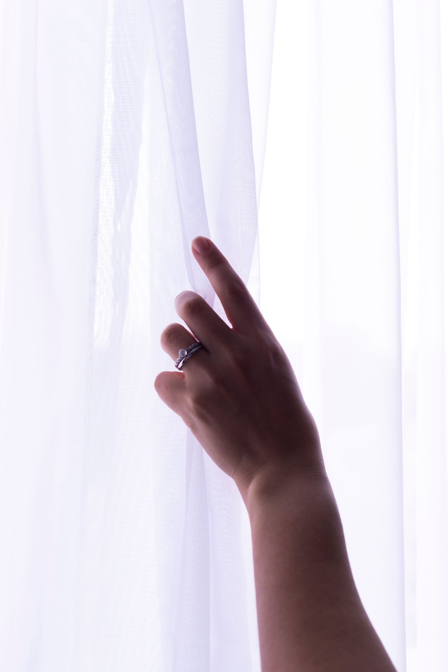 Hands reaching up towards sheer white curtains in gentle lighting.