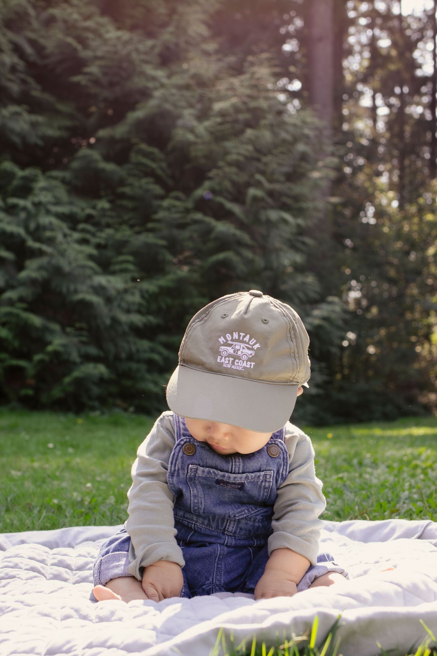Child wearing overalls and baseball cap resting on quilted blanket near evergreen trees.
Central Park Burnaby