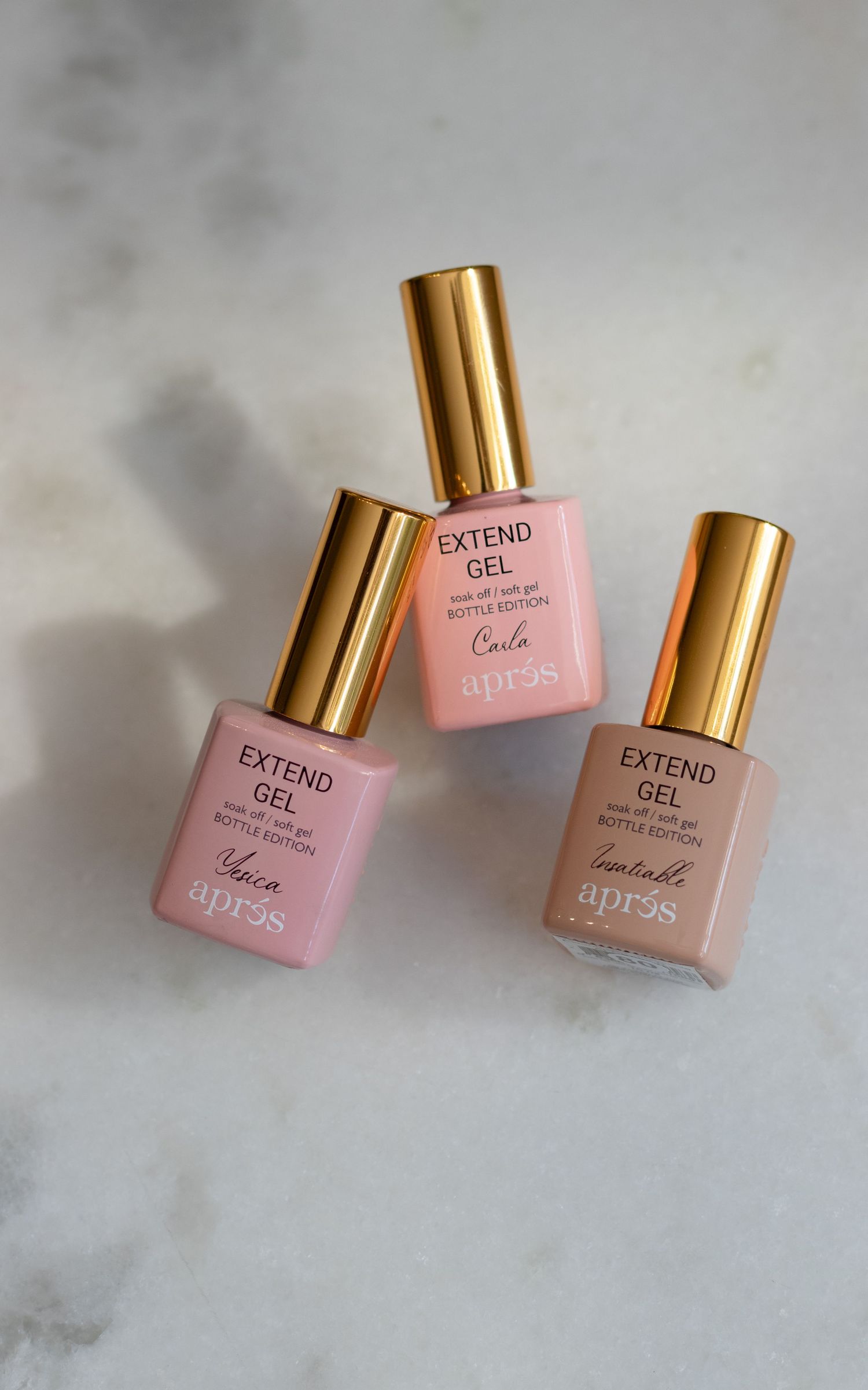 Pink nail polish bottles with gold caps arranged on a light gray marble surface.