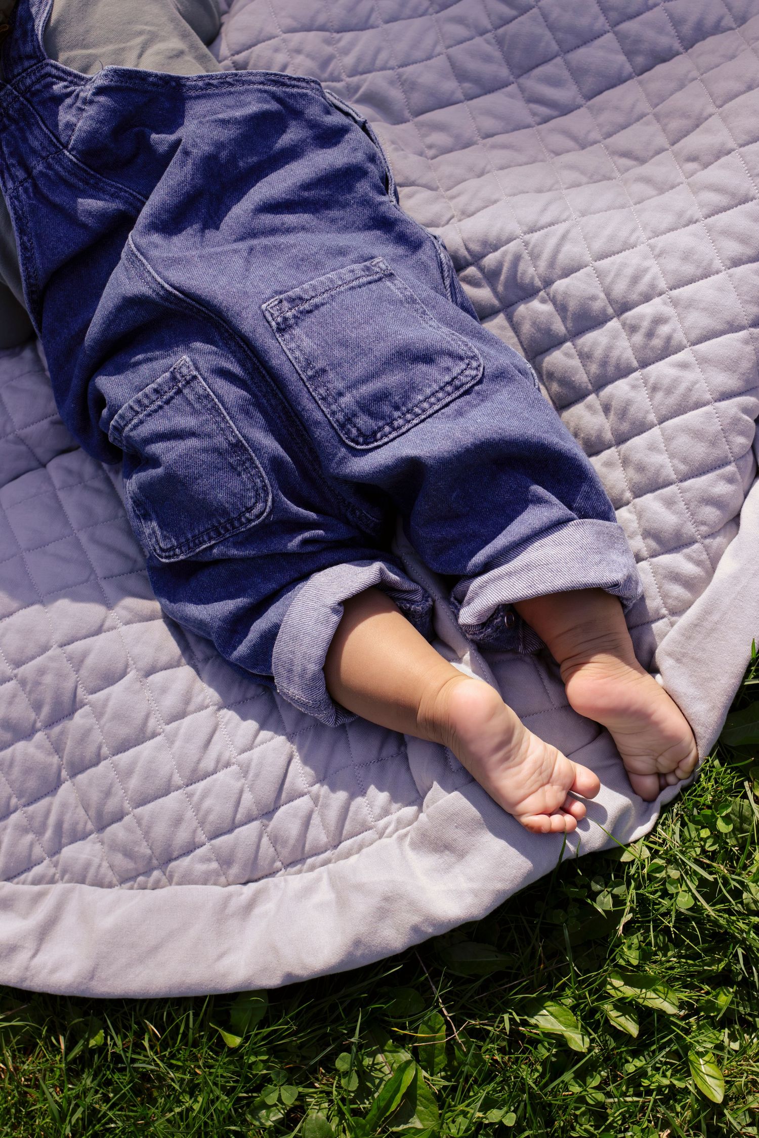 Tiny feet in denim overalls resting on gray quilted blanket against green grass.
Central Park Burnaby