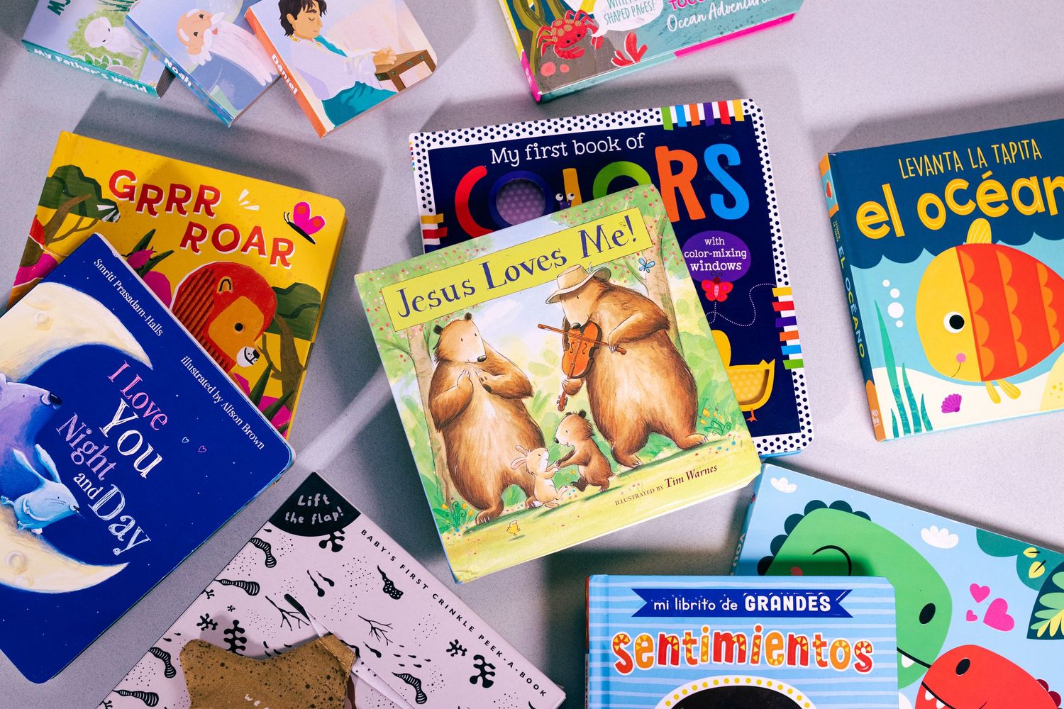 Colorful children's board books spread out, including Jesus Loves Me, Colors, and bilingual titles for toddlers.