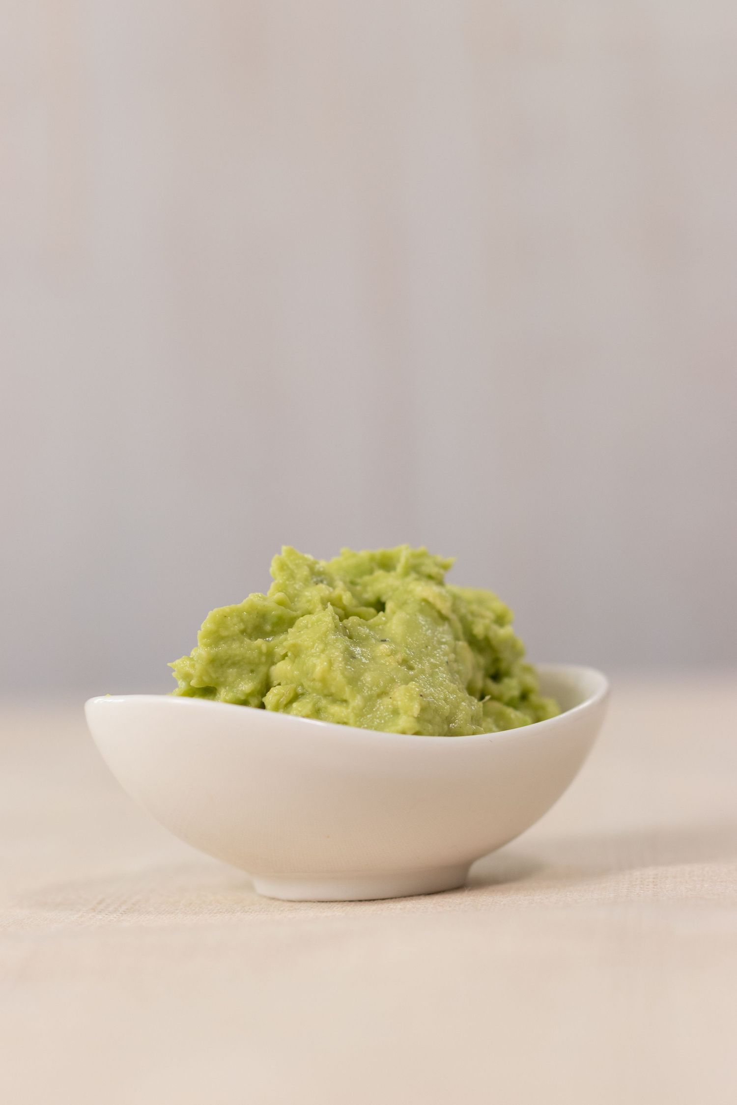 Creamy guacamole dip served in a white curved bowl on beige surface.