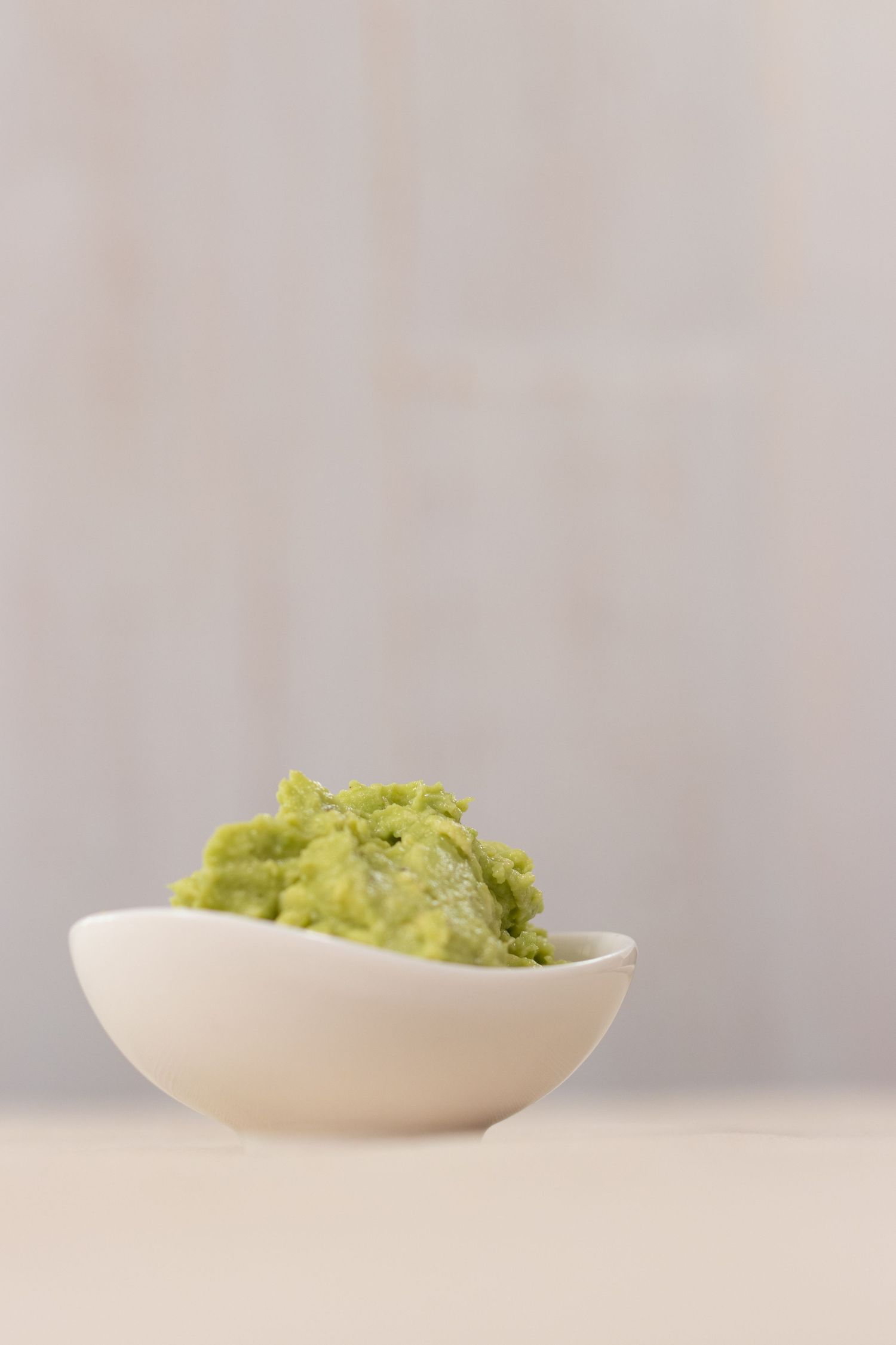 A white bowl filled with fresh guacamole on a light surface.