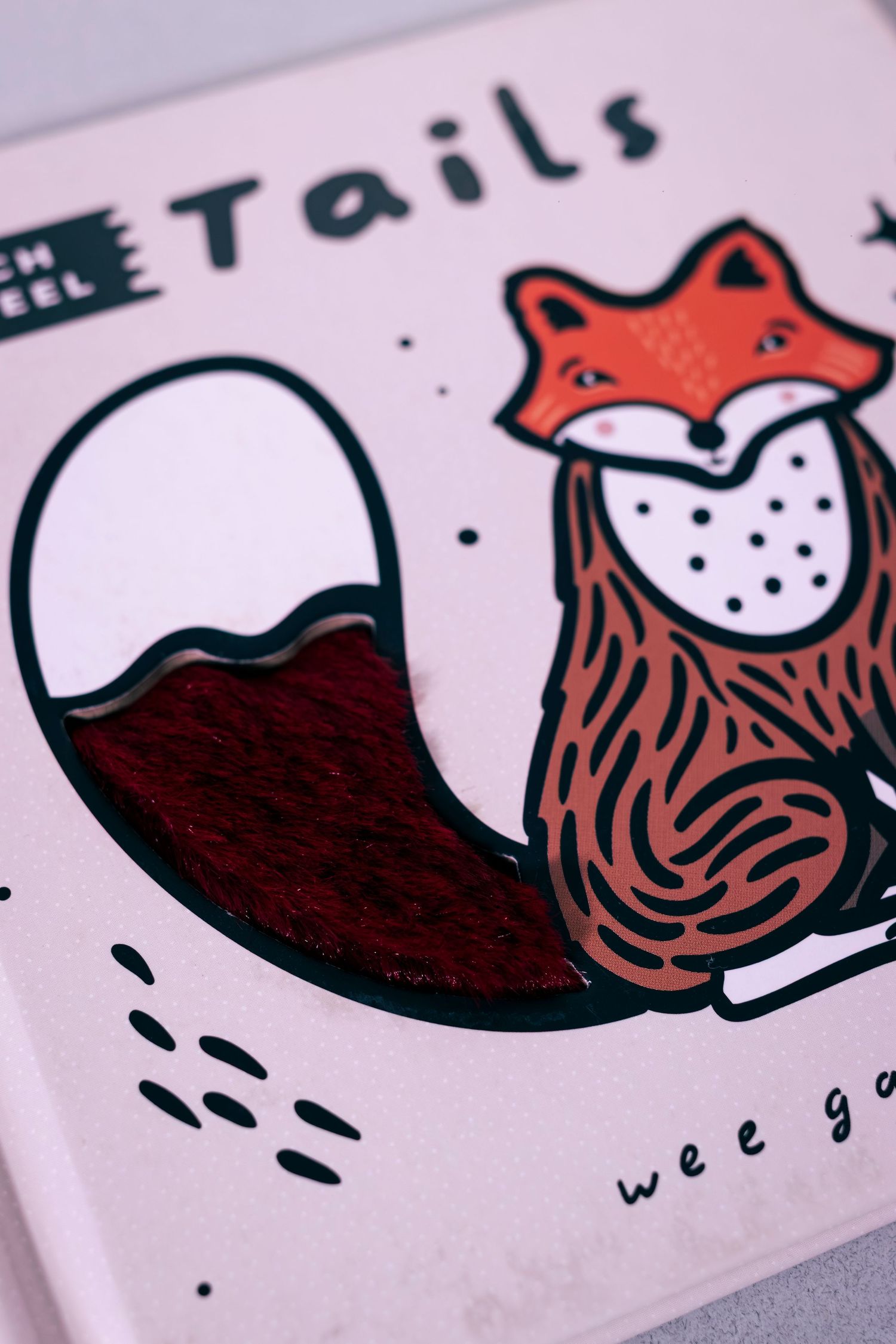 Close-up of a childrens touch and feel Tails book by Wee Gallery featuring a illustrated fox with a fluffy tail.