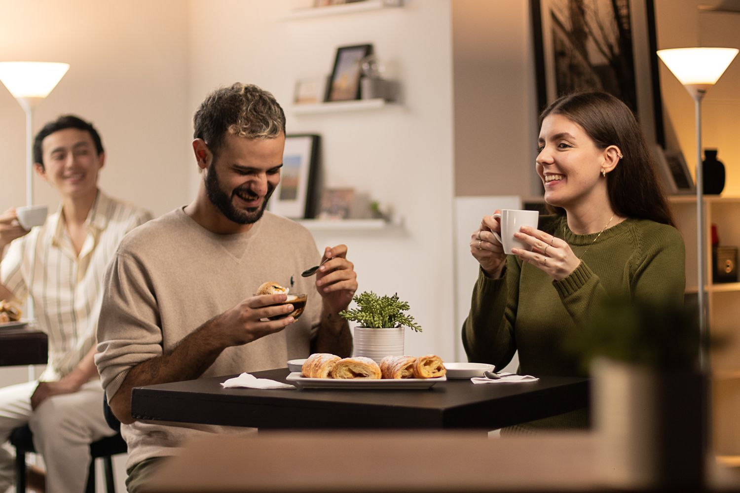 Friends gathered around table enjoying coffee and conversation in warm lighting.