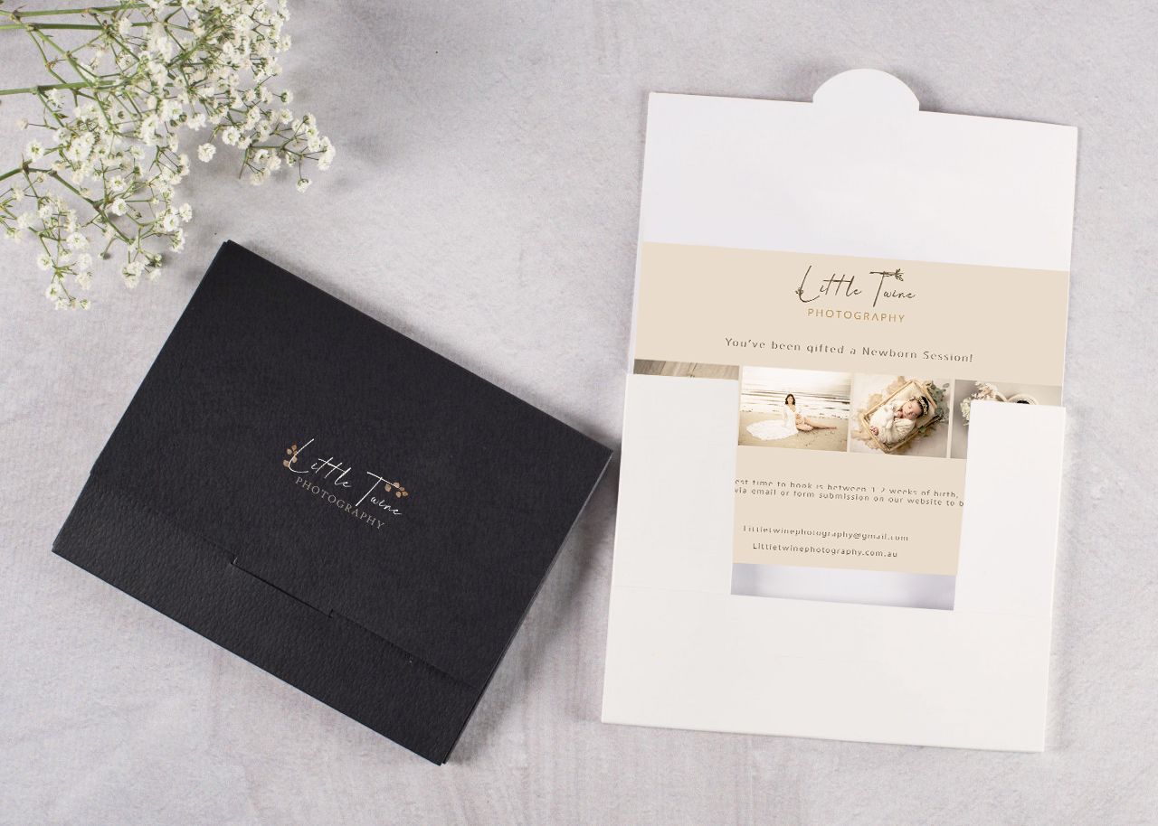 Elegant black and white business cards and stationery displayed with delicate white flowers on a gray marble surface.