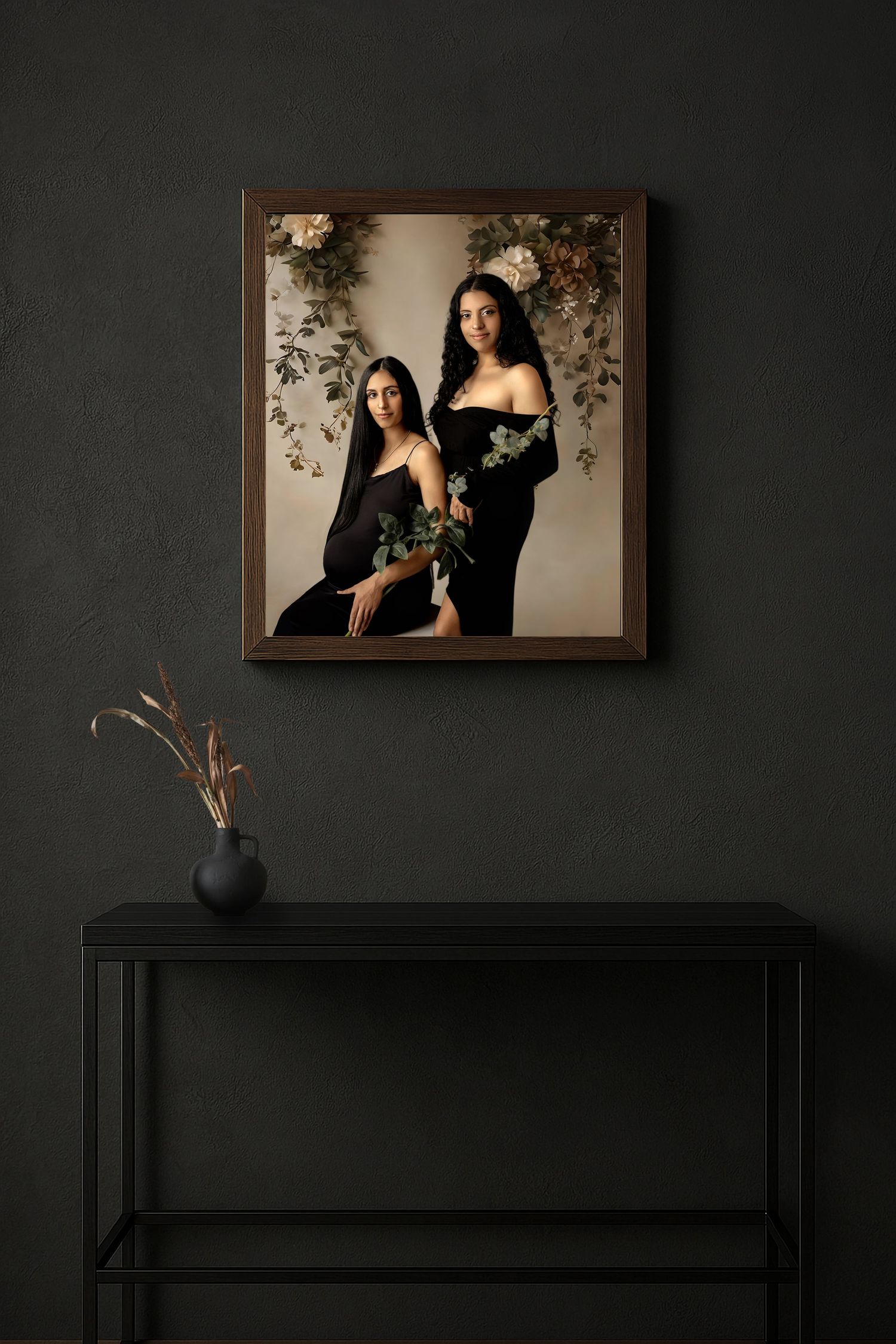 Two women in black dresses pose elegantly with flowers in a framed portrait hanging above a black console table.