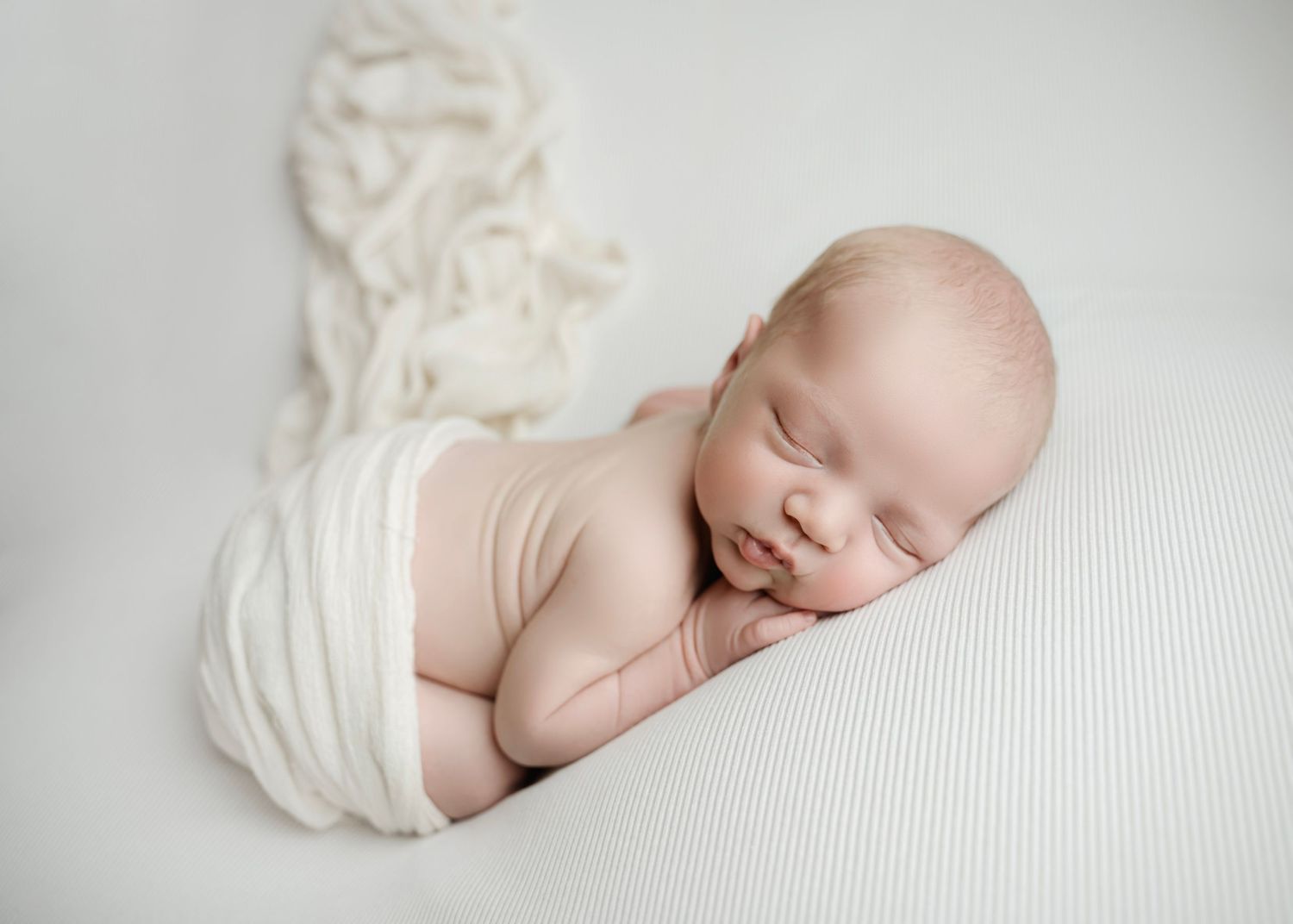 Sleeping newborn baby wrapped in white swaddle on white background in professional newborn photography.