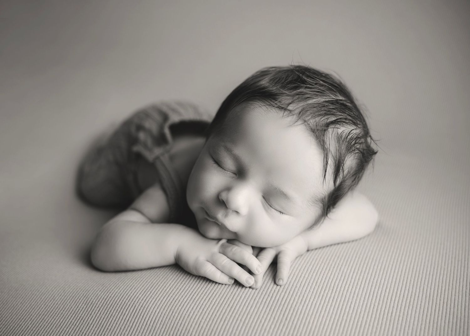 Black and white newborn photography of a sleeping baby resting chin on hands, peaceful portrait.