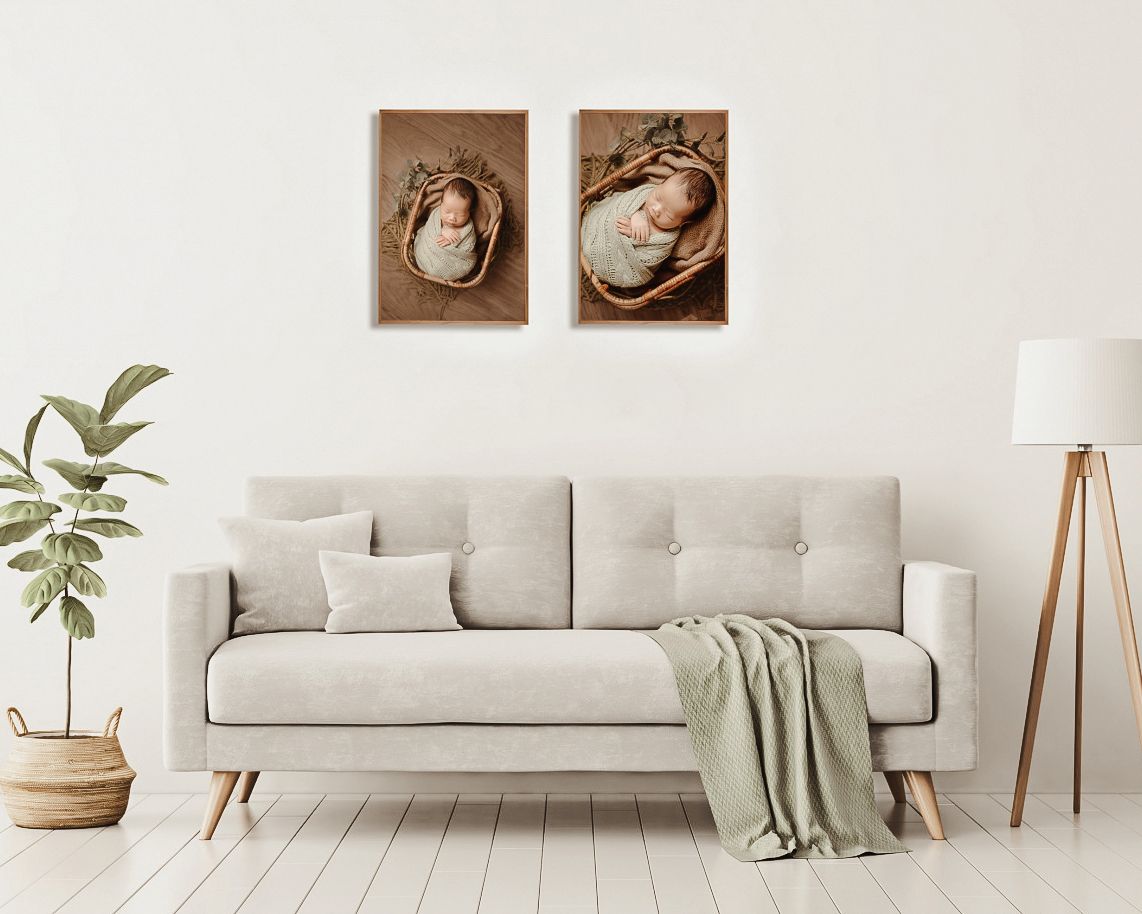 A modern living room with a beige sofa displaying two framed newborn portrait photos on a white wall above.