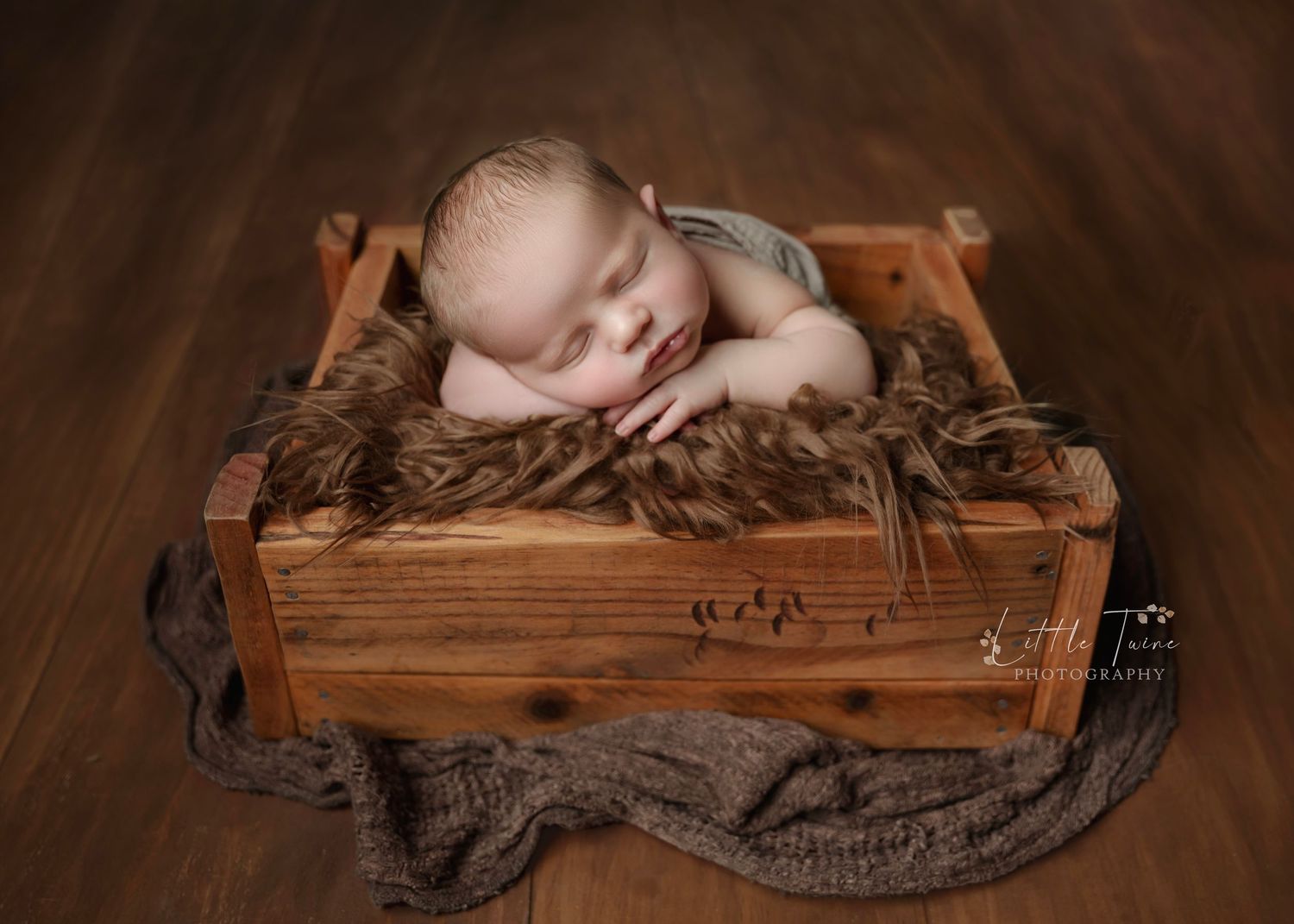 Sleeping newborn baby posed in a rustic wooden crate with brown fur, professional newborn photography.