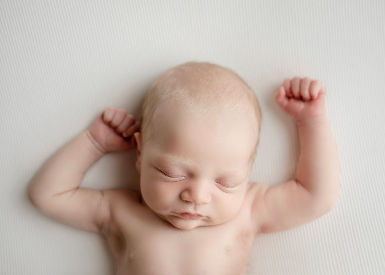 Peaceful newborn baby sleeping on white background with arms raised, captured in professional newborn photography.