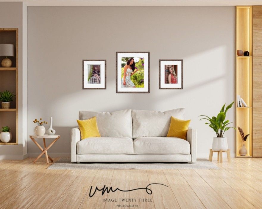 A modern living room with a white sofa, yellow pillows, and three framed portrait photos displayed on a neutral wall.