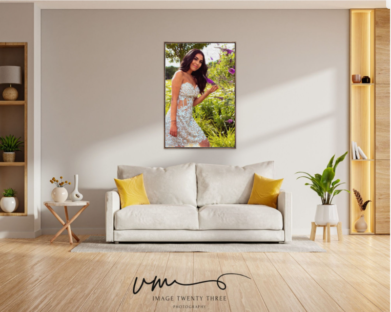 A framed portrait photo of a young woman in a floral dress hangs above a white sofa in a modern living room.
