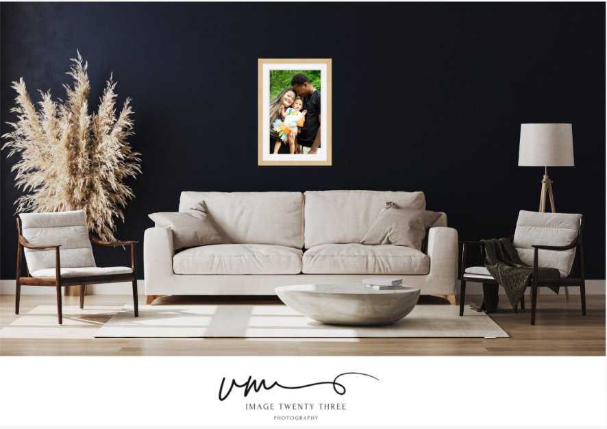 Elegant living room with dark walls featuring a framed family portrait above a beige sofa, flanked by pampas grass and modern chairs.