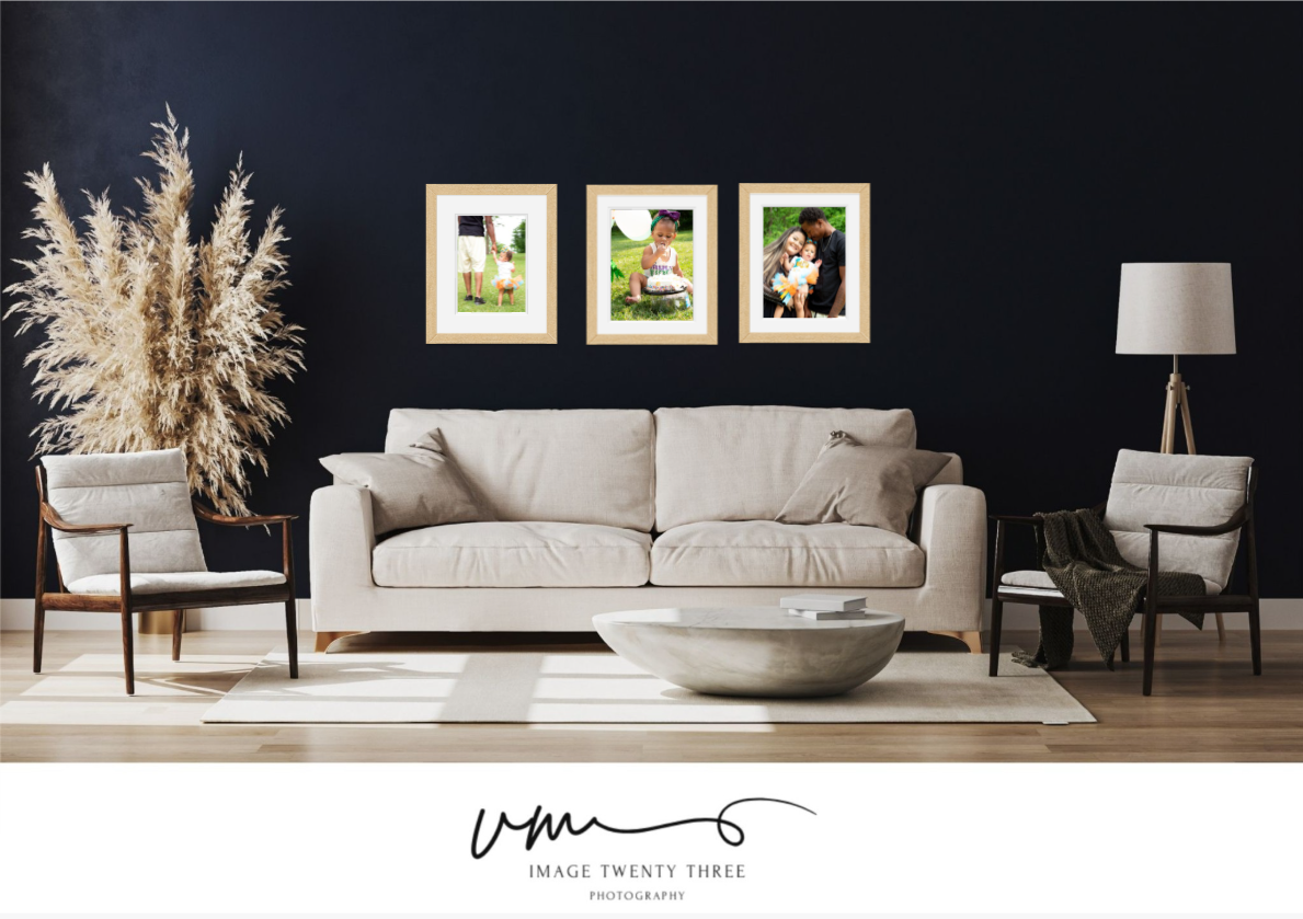 Modern living room with a beige sofa, dark walls, and three framed family photos displayed in gold frames above the couch.