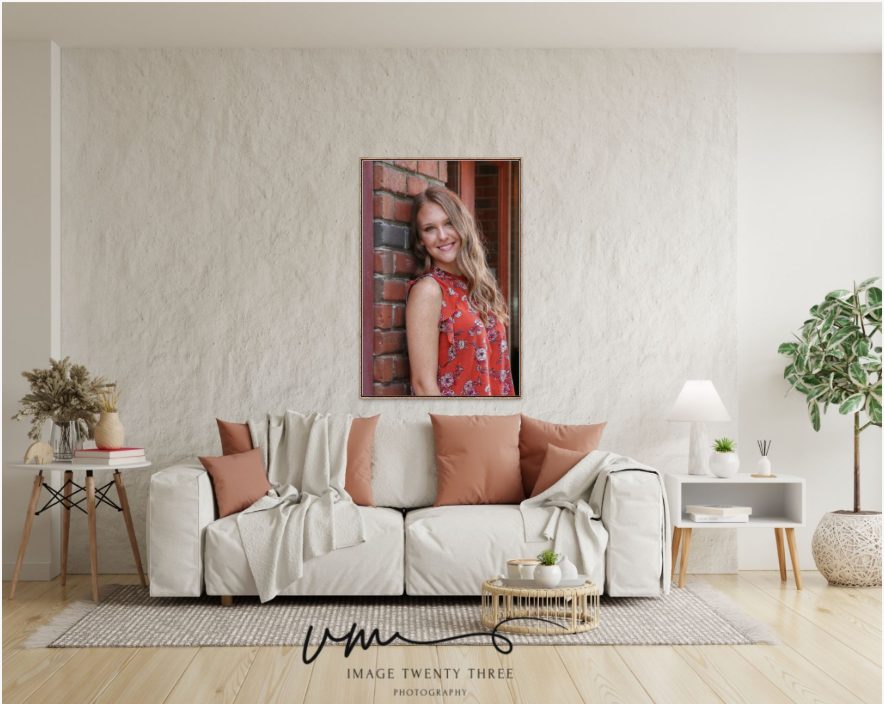 A smiling teenage girl in a red dress poses against a brick wall in a large canvas print displayed above a white sofa.