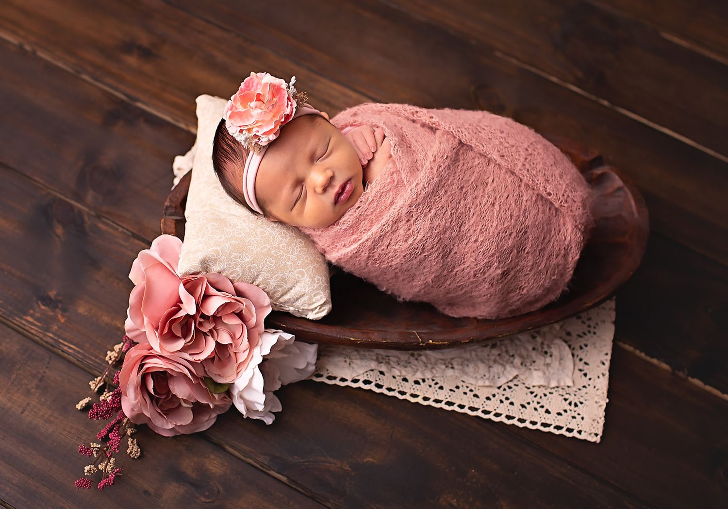 Baby girl wrapped up in a pink wrap posed in a bowl with flowers for newborn session
