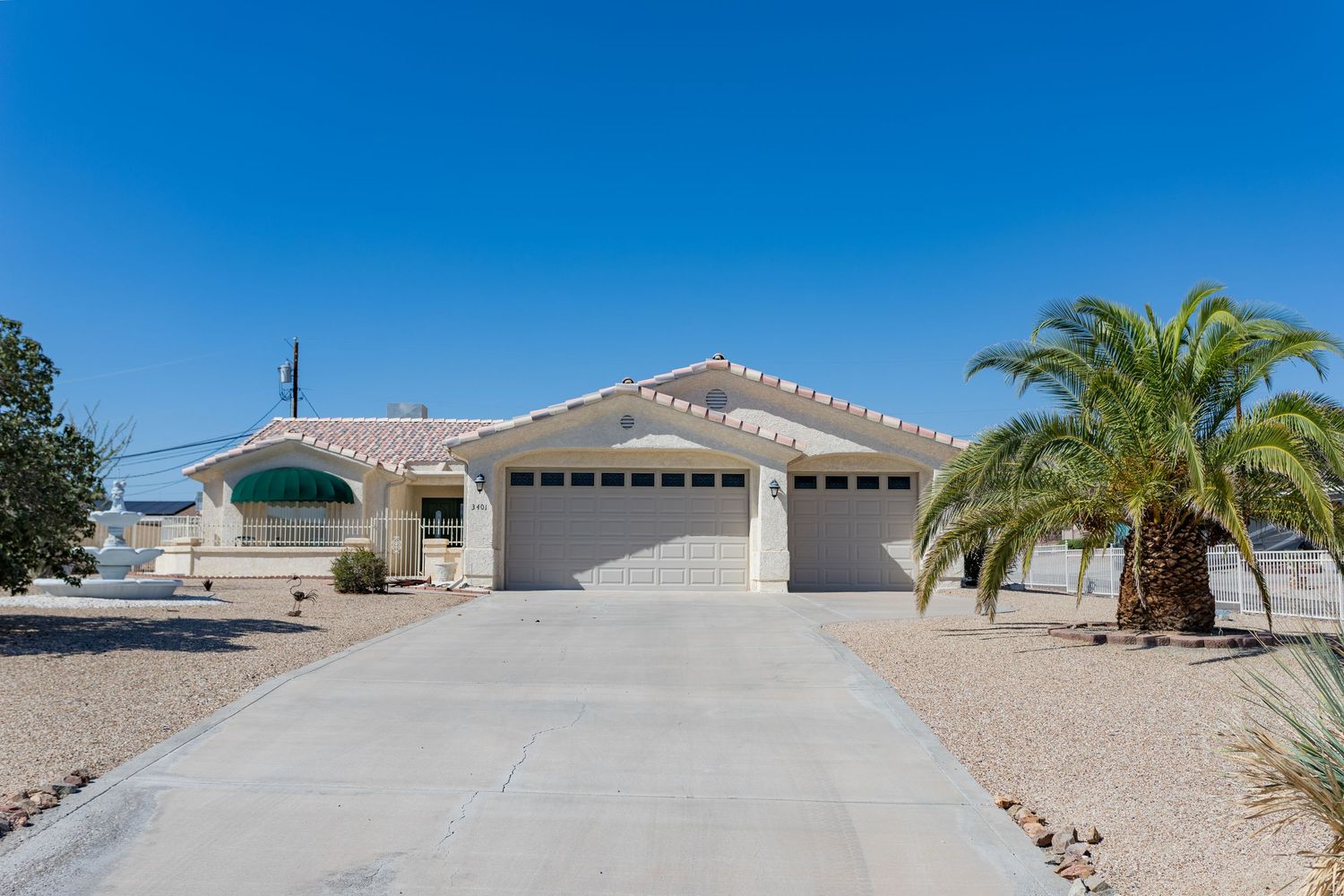 A panoramic view of a desert property with a tan-colored single-story home and palm trees in the front yard.