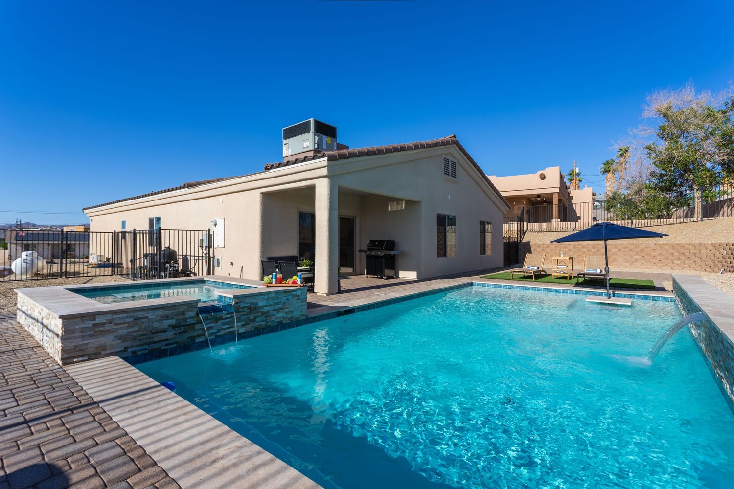 A large rectangular swimming pool with crystal clear turquoise water surrounded by stone pavers and desert landscaping.