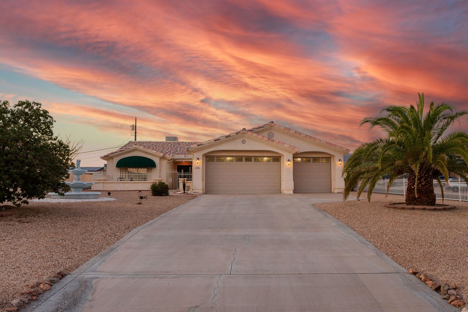 A desert home with two-car garage and palm tree under vibrant pink and orange sunset sky in Arizona.