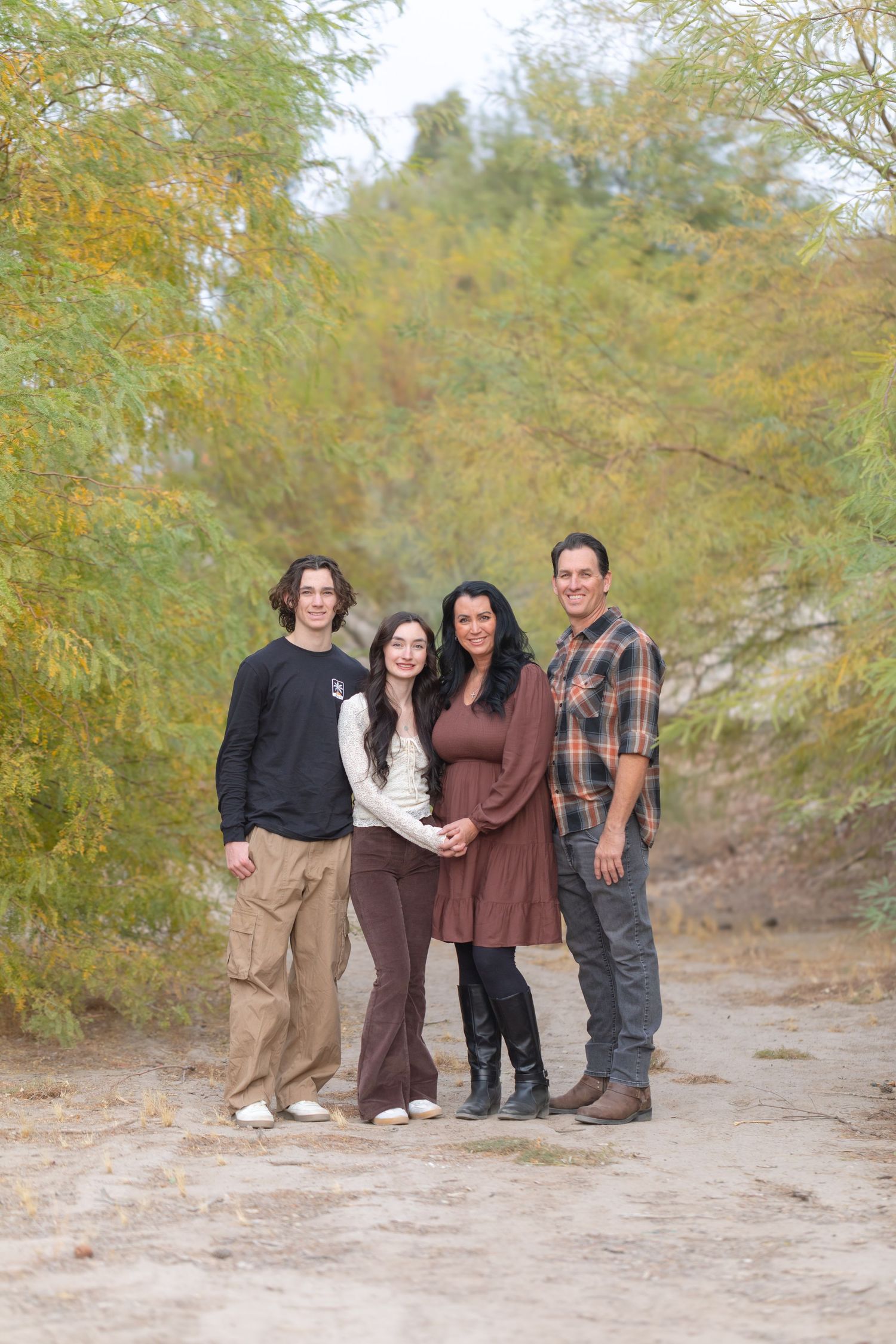 Four people pose together outdoors on a dirt path surrounded by autumn trees with yellow-green foliage in Lake Havasu City Arizona