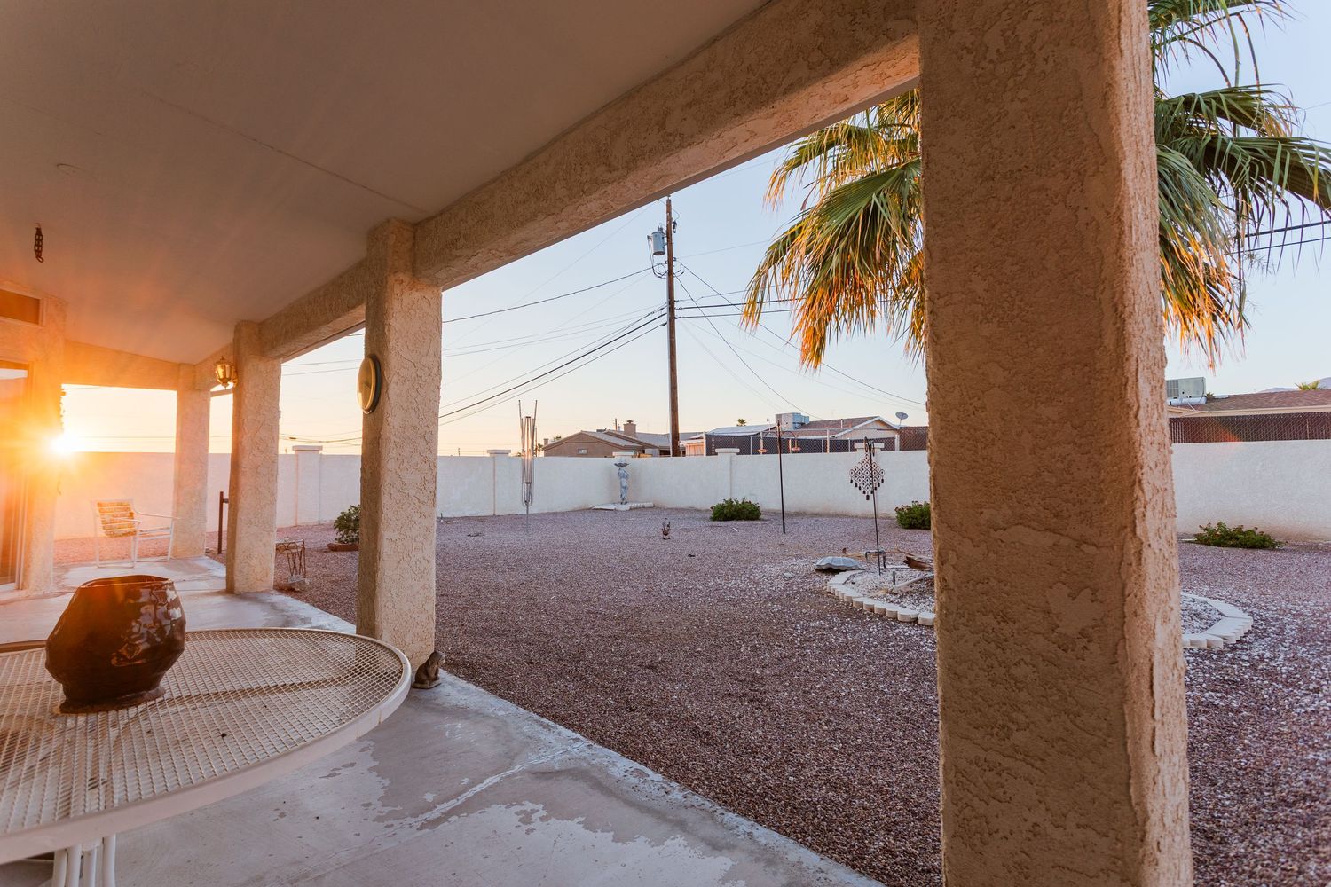 A long pillar-lined patio walkway with desert landscaping and palm trees at sunset creates a serene outdoor atmosphere.