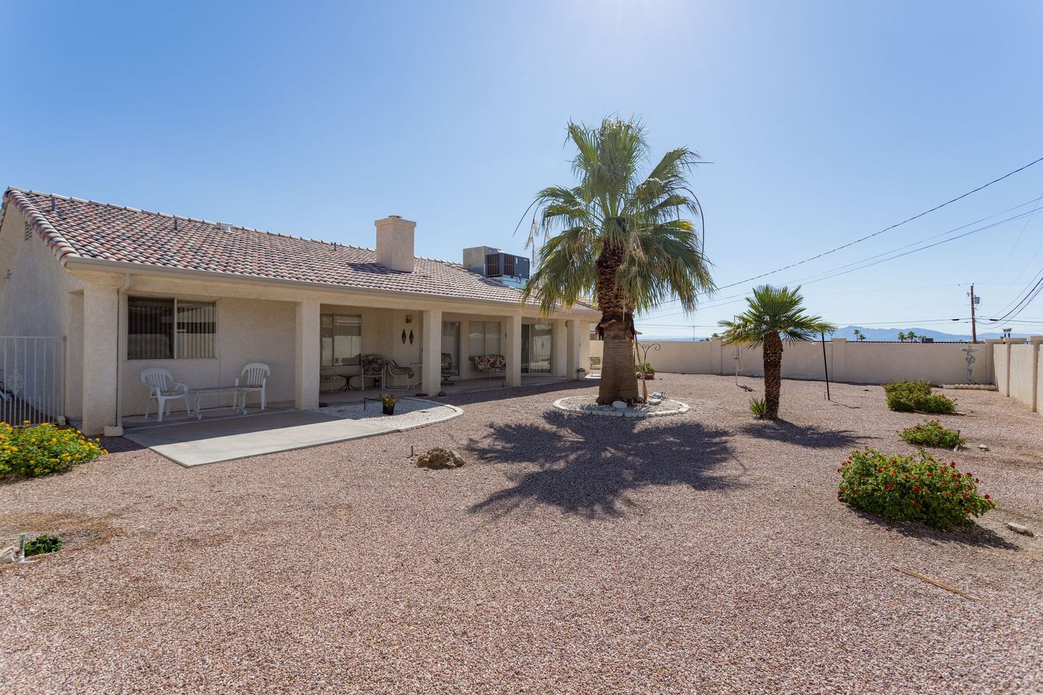 Desert ranch-style home with beige exterior, palm trees and gravel landscaping in a sunny southwestern setting.